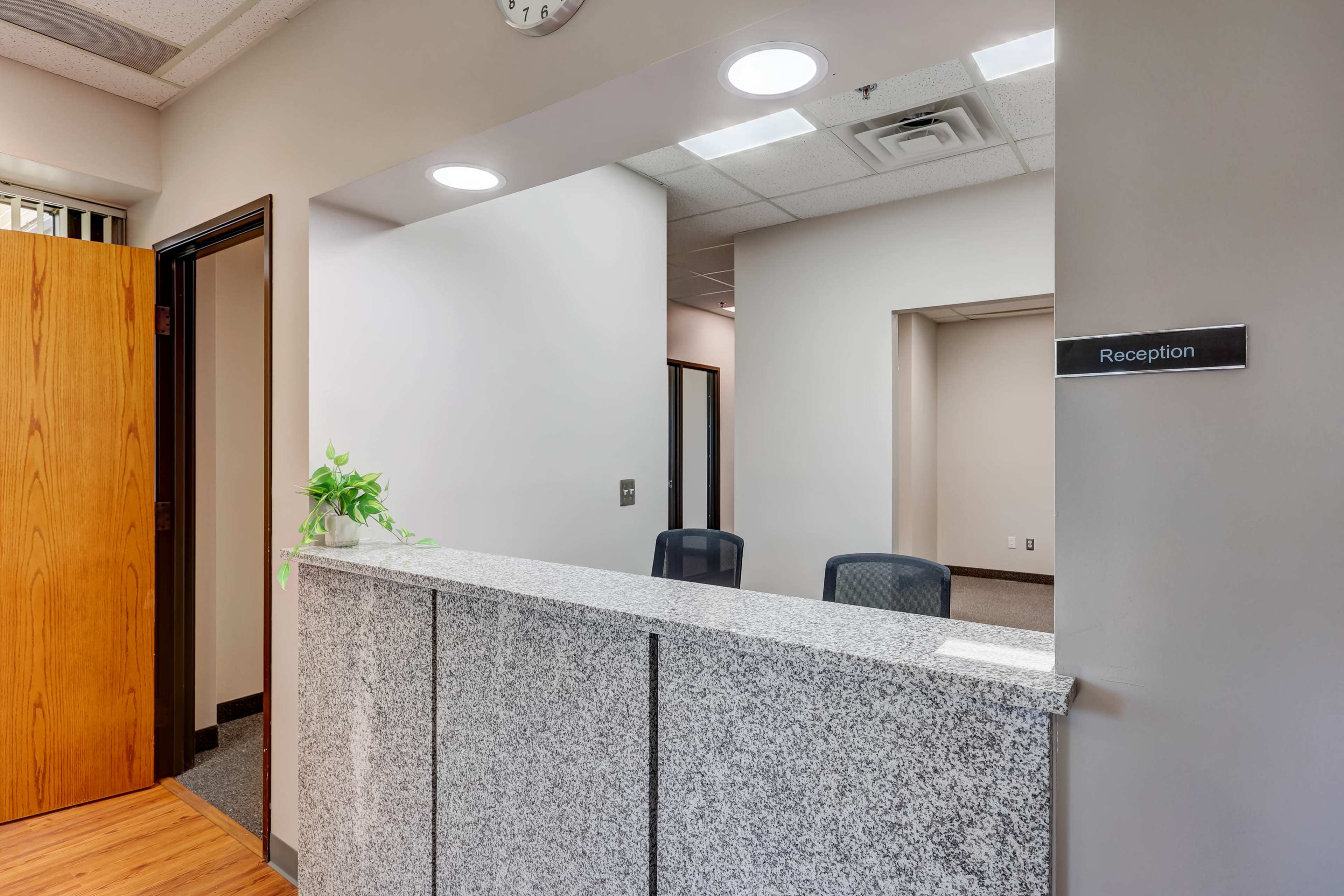 A reception area with a granite front desk, two black chairs, and a sign indicating "Reception."