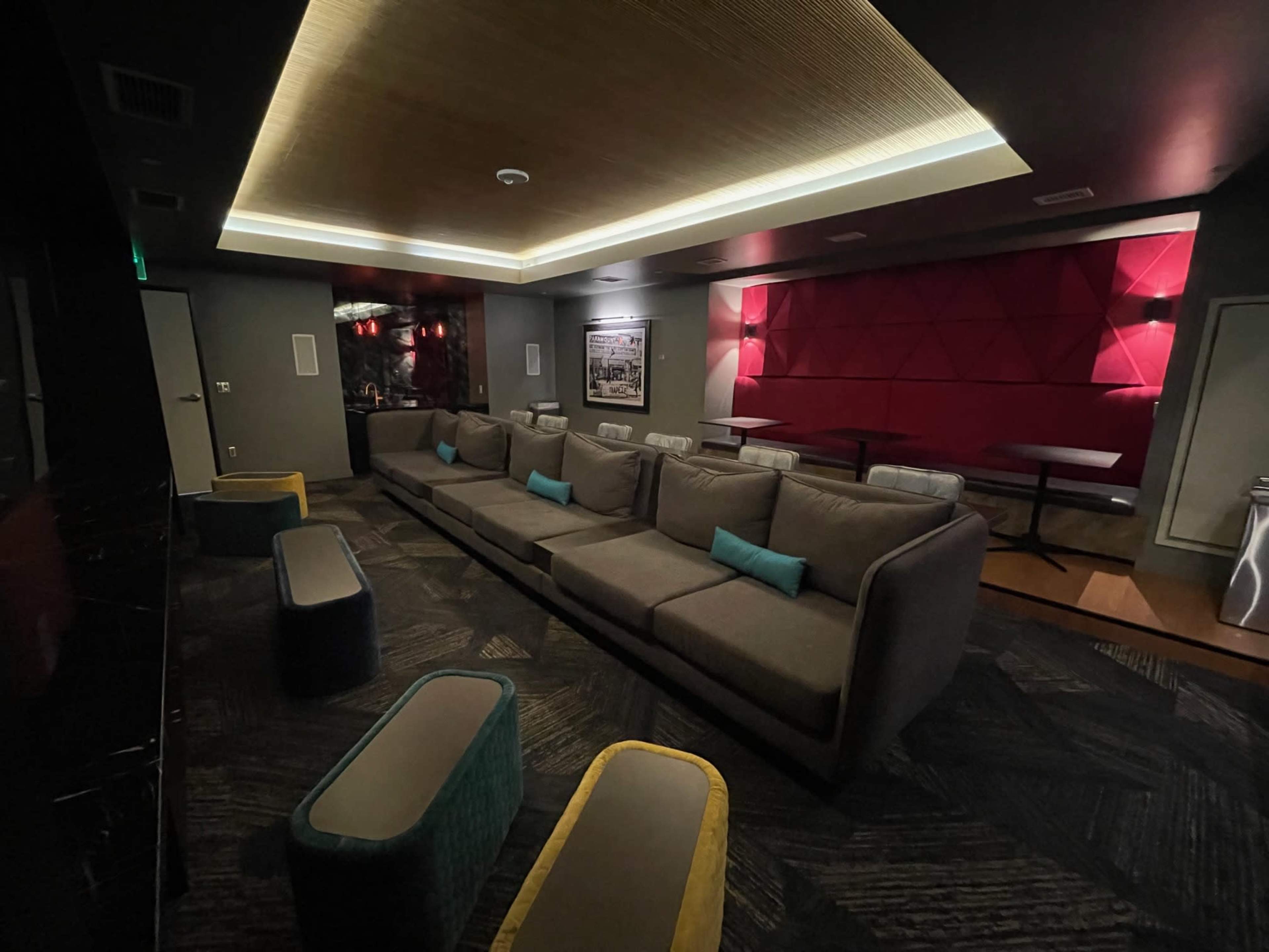 A modern lounge area with a large gray sectional sofa and colorful stools under soft lighting.