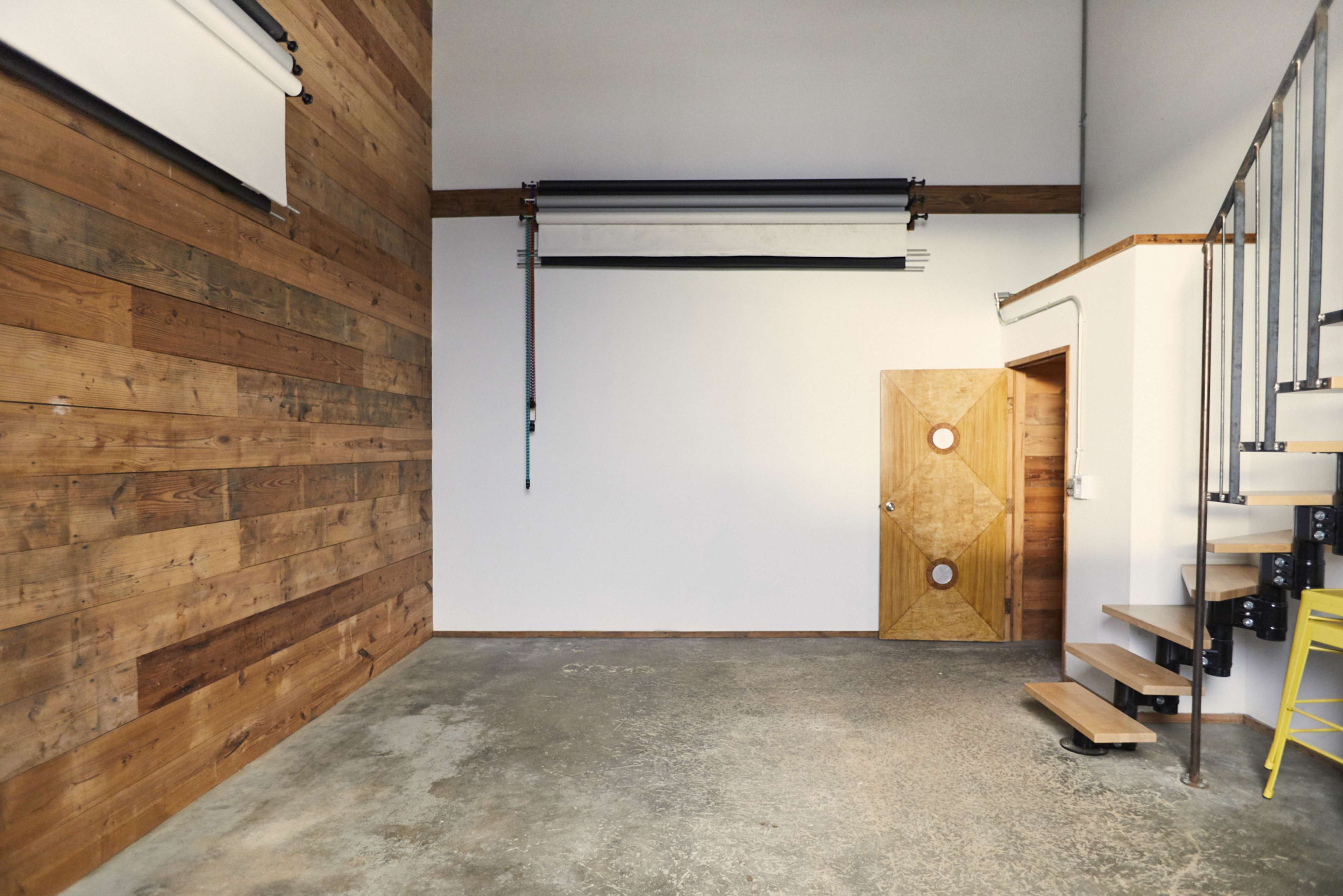 The image shows an interior space with a wooden wall, a white wall, a staircase, and a door featuring circular handles.