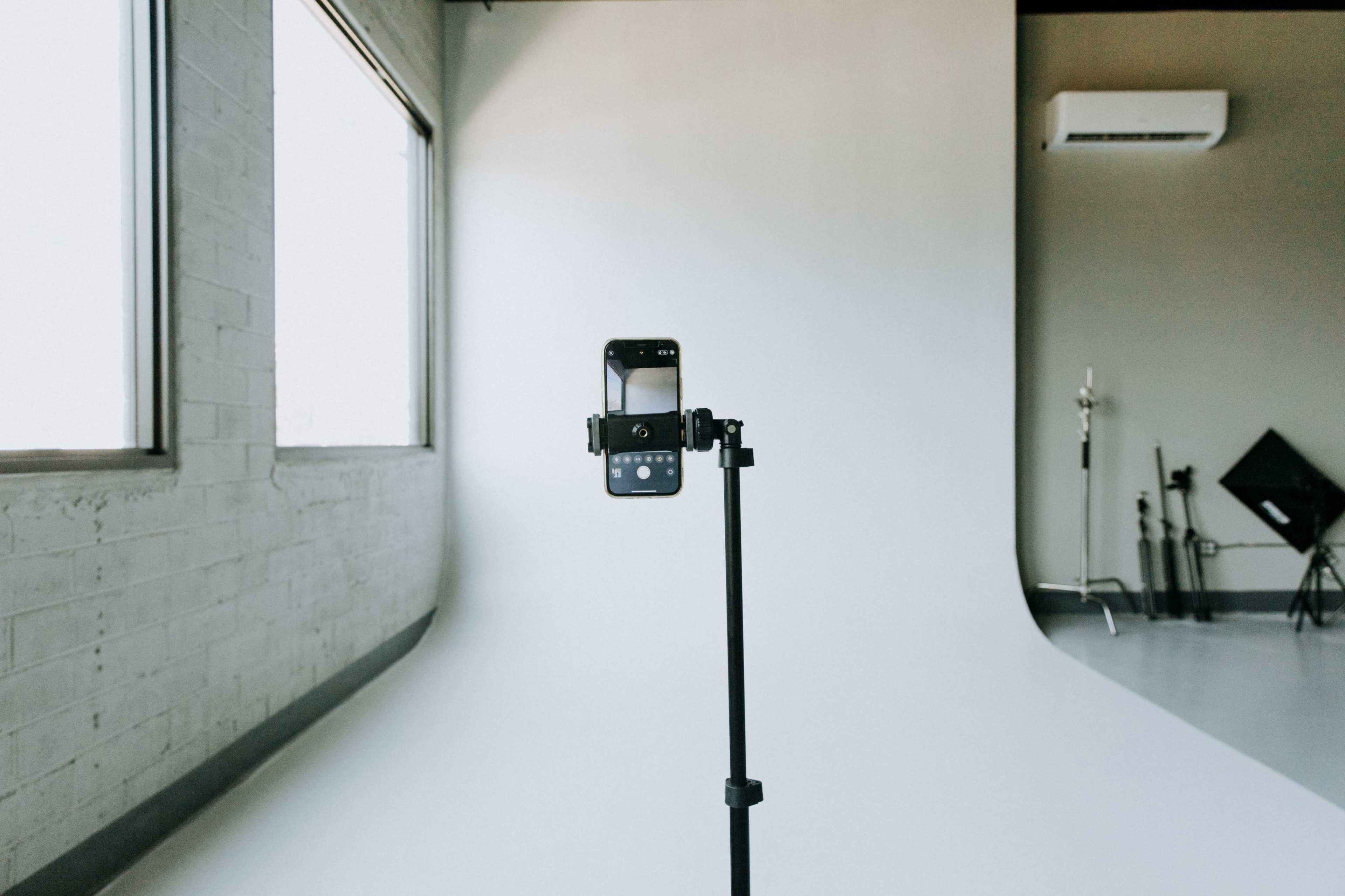 A smartphone is mounted on a stand facing a plain white backdrop in a photography studio.