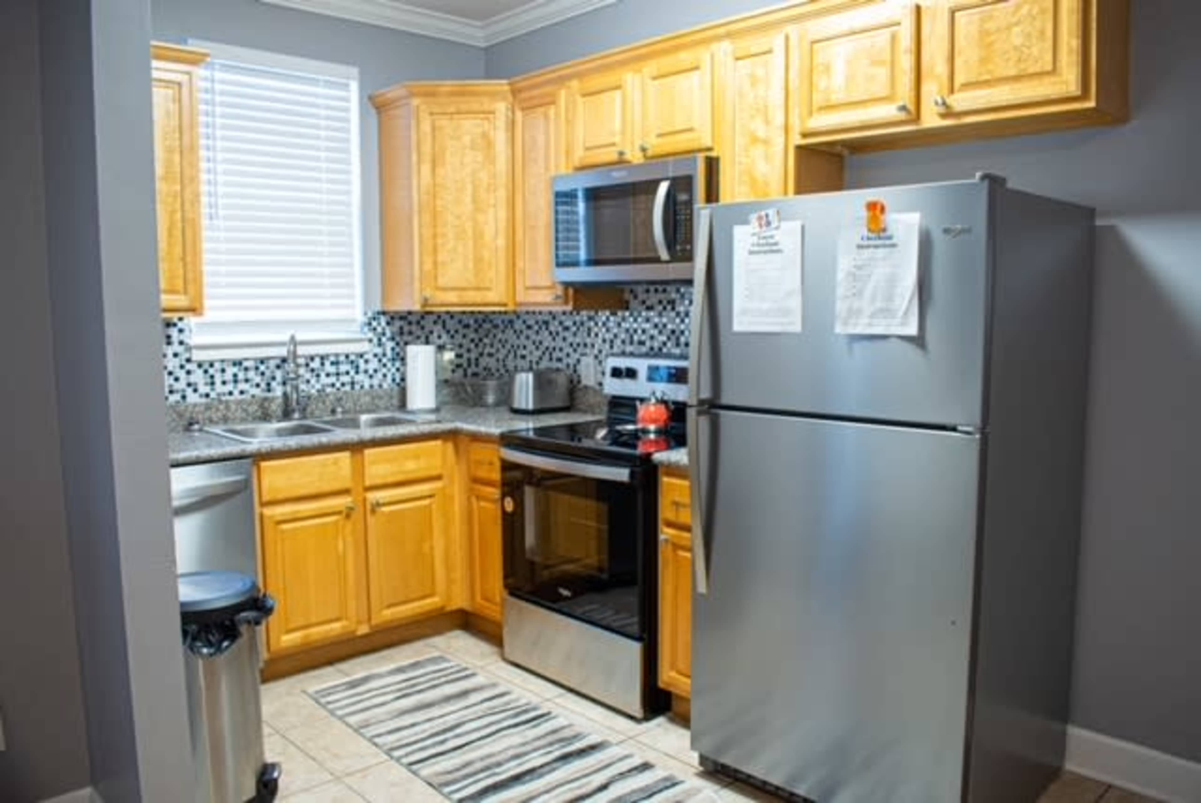A kitchen with wooden cabinets, stainless steel appliances, a silver refrigerator, and a tile floor.