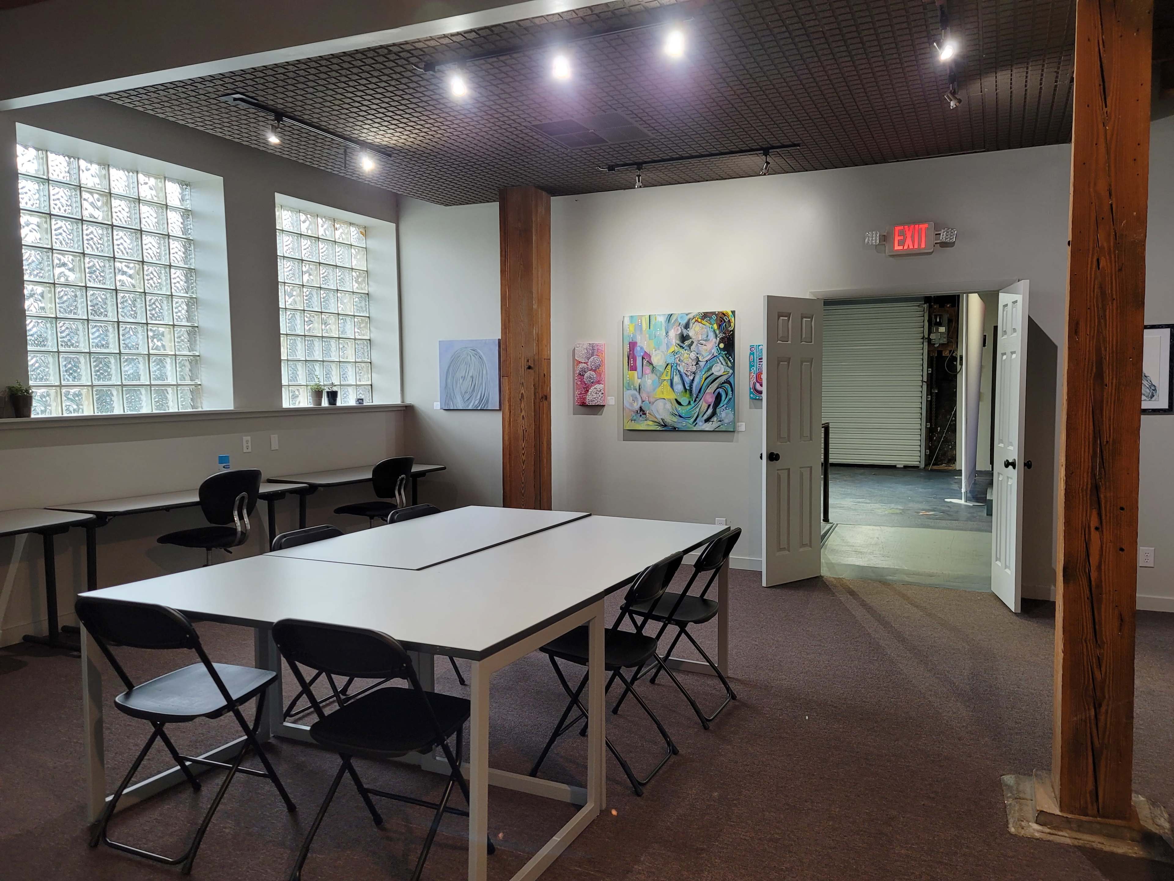 A spacious room with a long table surrounded by black chairs, decorated with artwork on the walls and a doorway leading to another area.