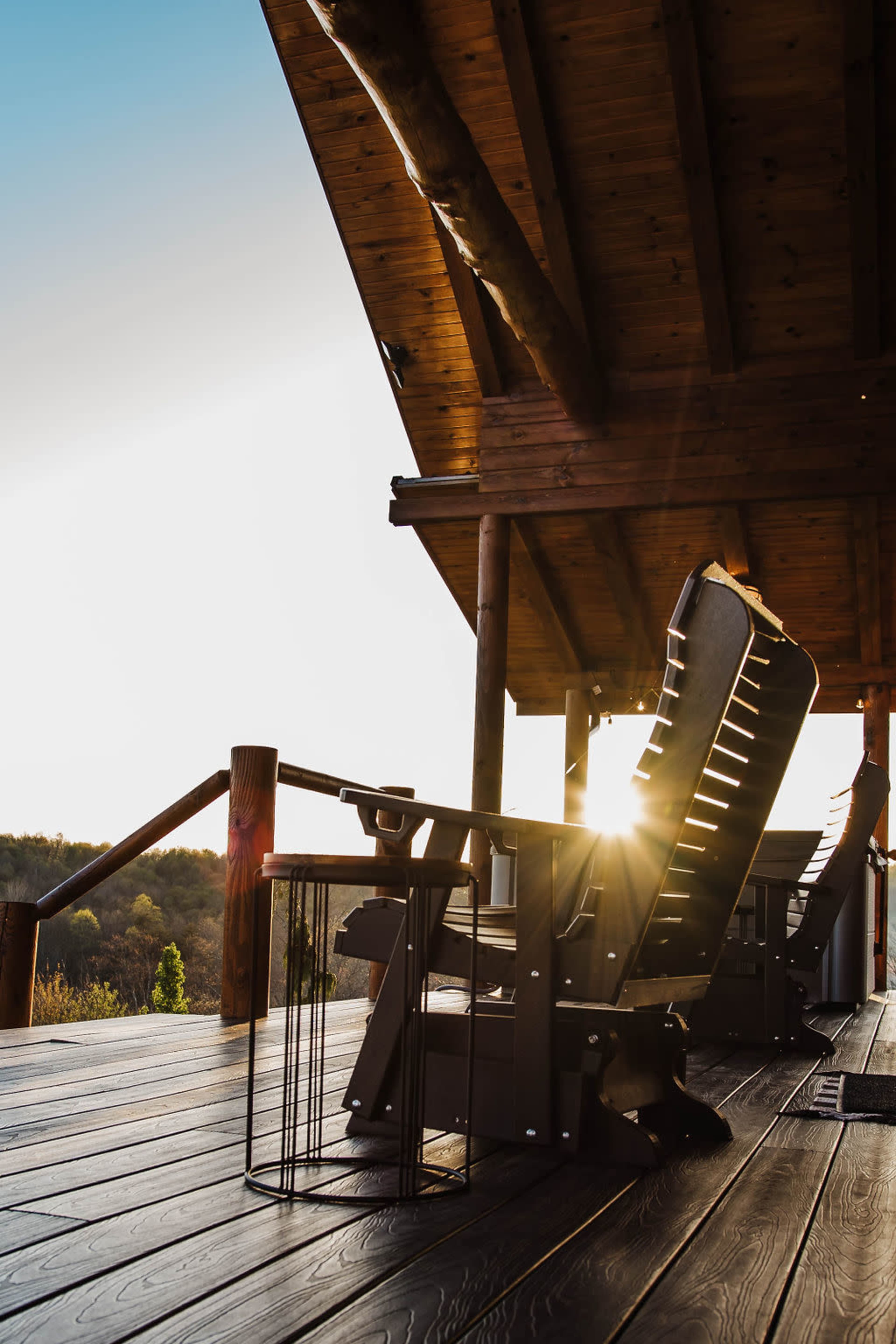 The image shows a wooden deck with rocking chairs and a small side table, illuminated by the sunset in the background.