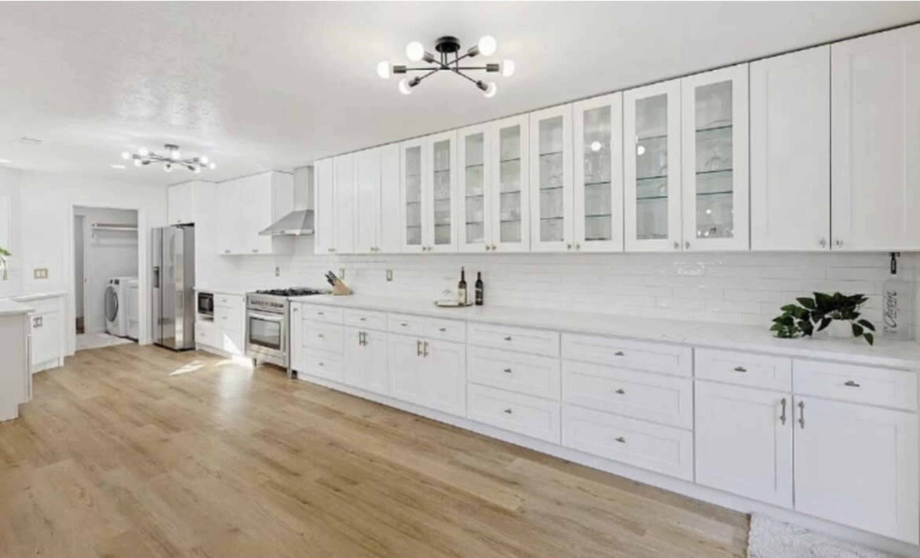 The image shows a modern kitchen featuring white cabinets, a large island, stainless steel appliances, and wooden flooring.