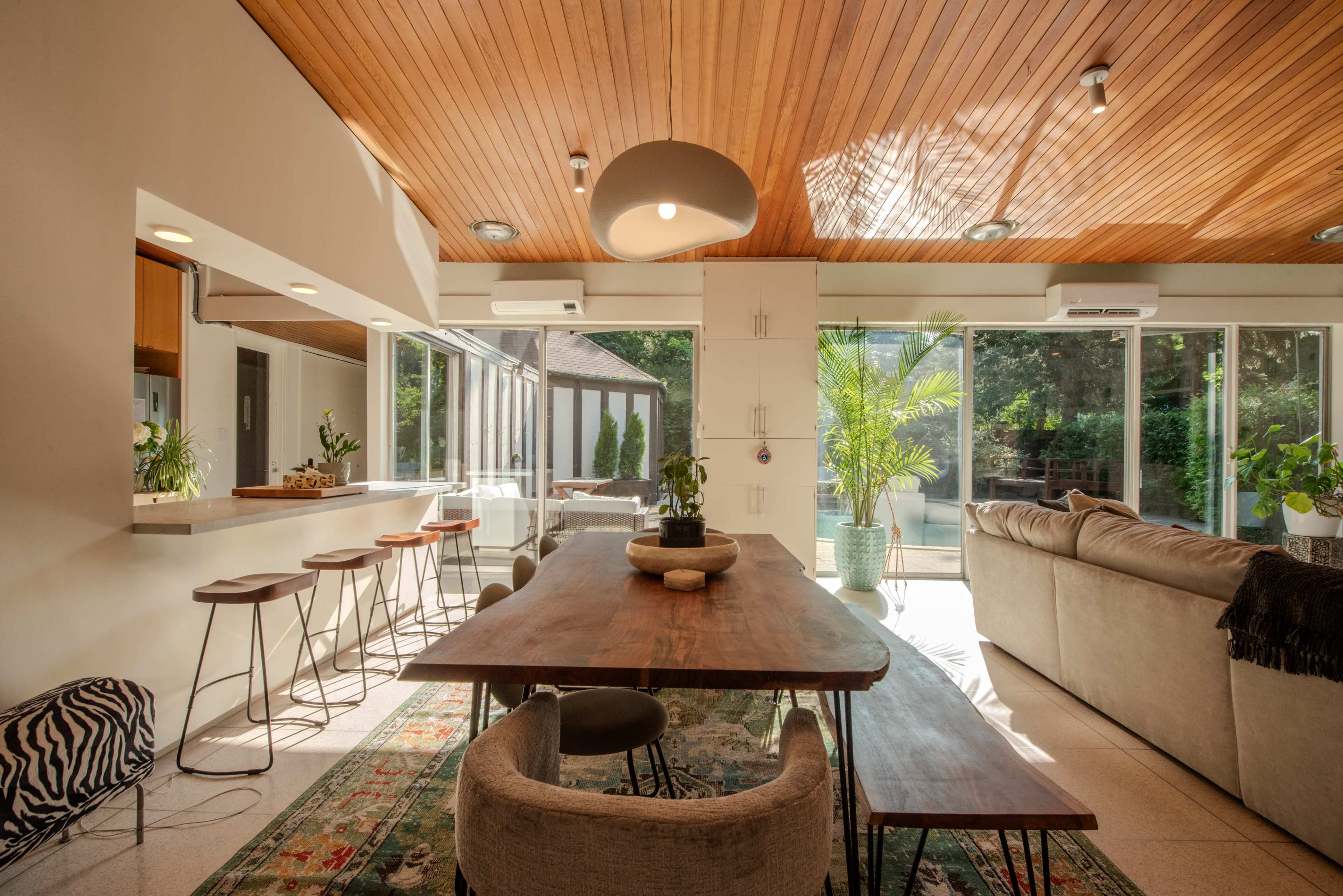 A spacious dining area features a wooden table surrounded by chairs, with large windows allowing natural light to illuminate the space.