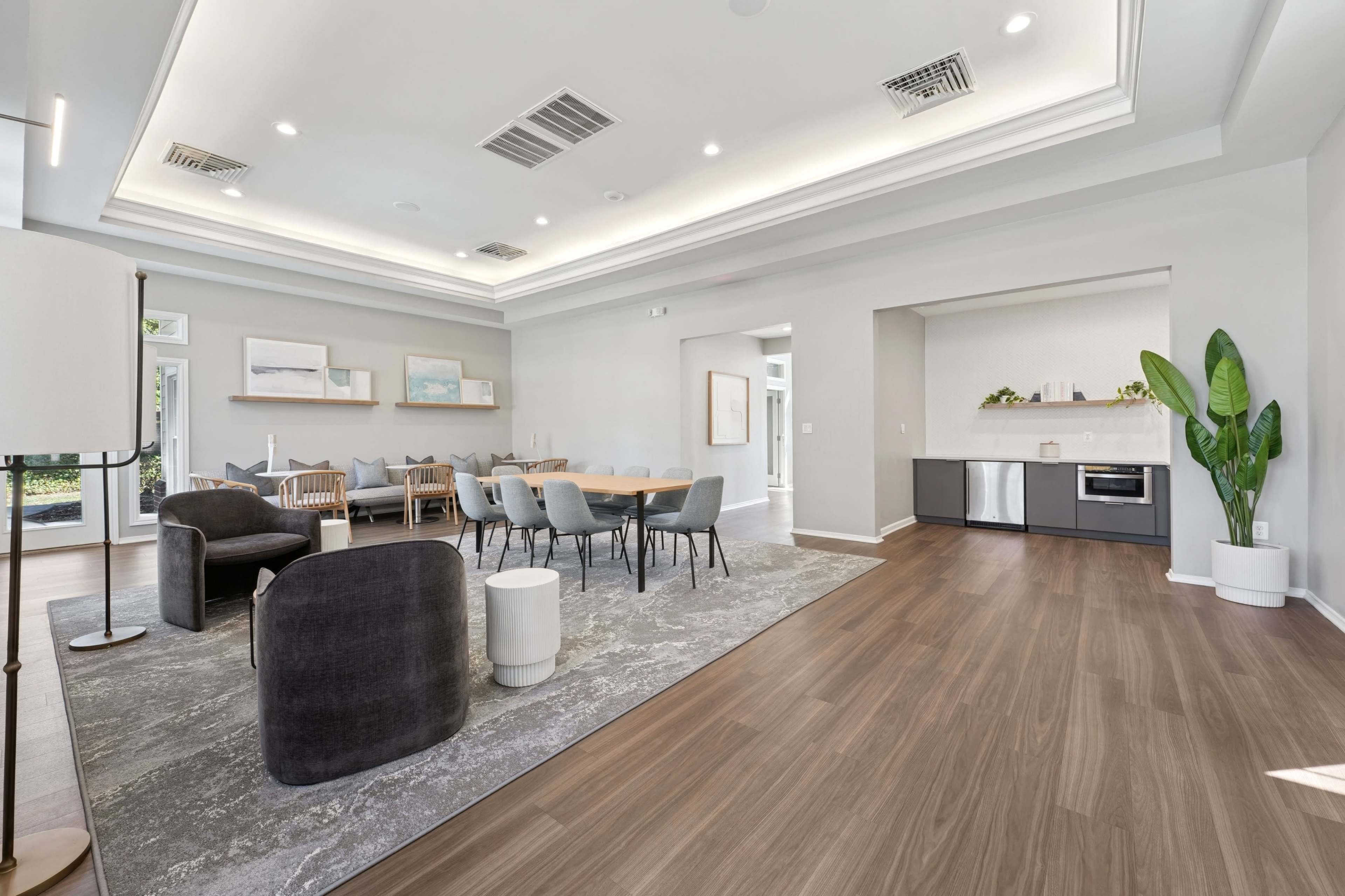 The image shows a modern, open-concept living space that features a dining area with a large table, comfortable seating, and a kitchen area with appliances.