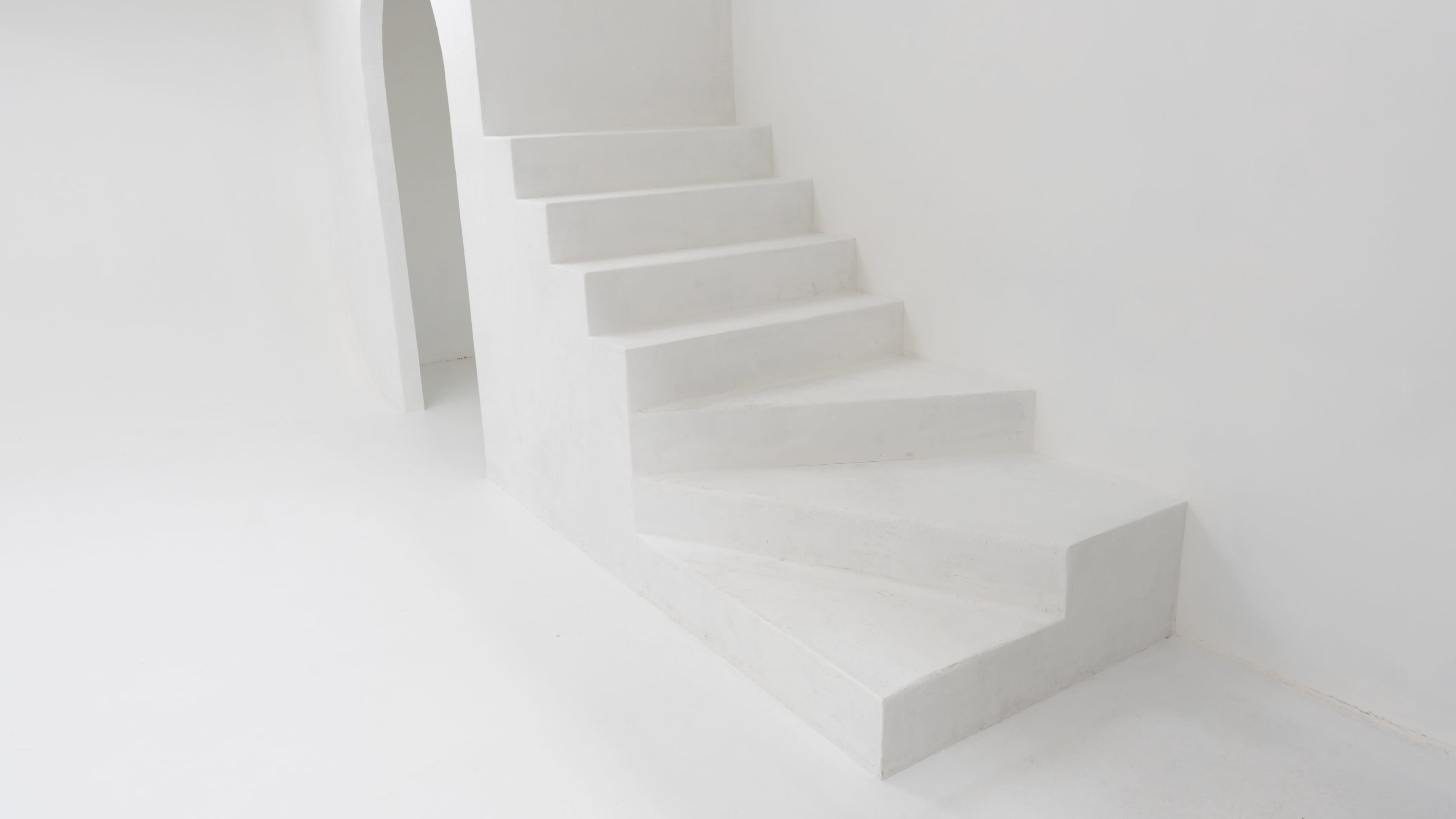 A set of white, minimalist stairs curves gently upward against a plain white background.