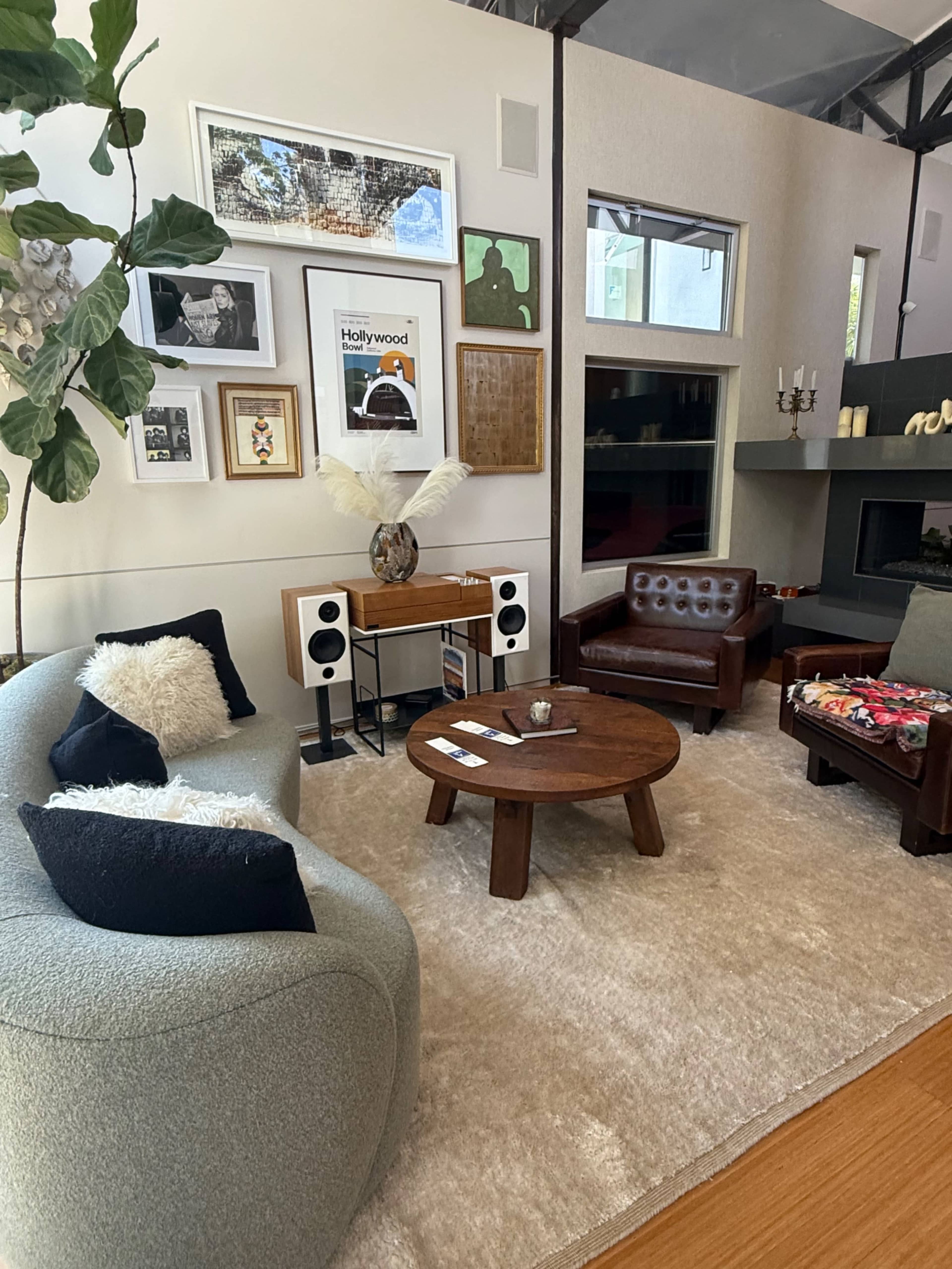 The image shows a living room with two different styled sofas, a round coffee table, wall art, and a tall plant.