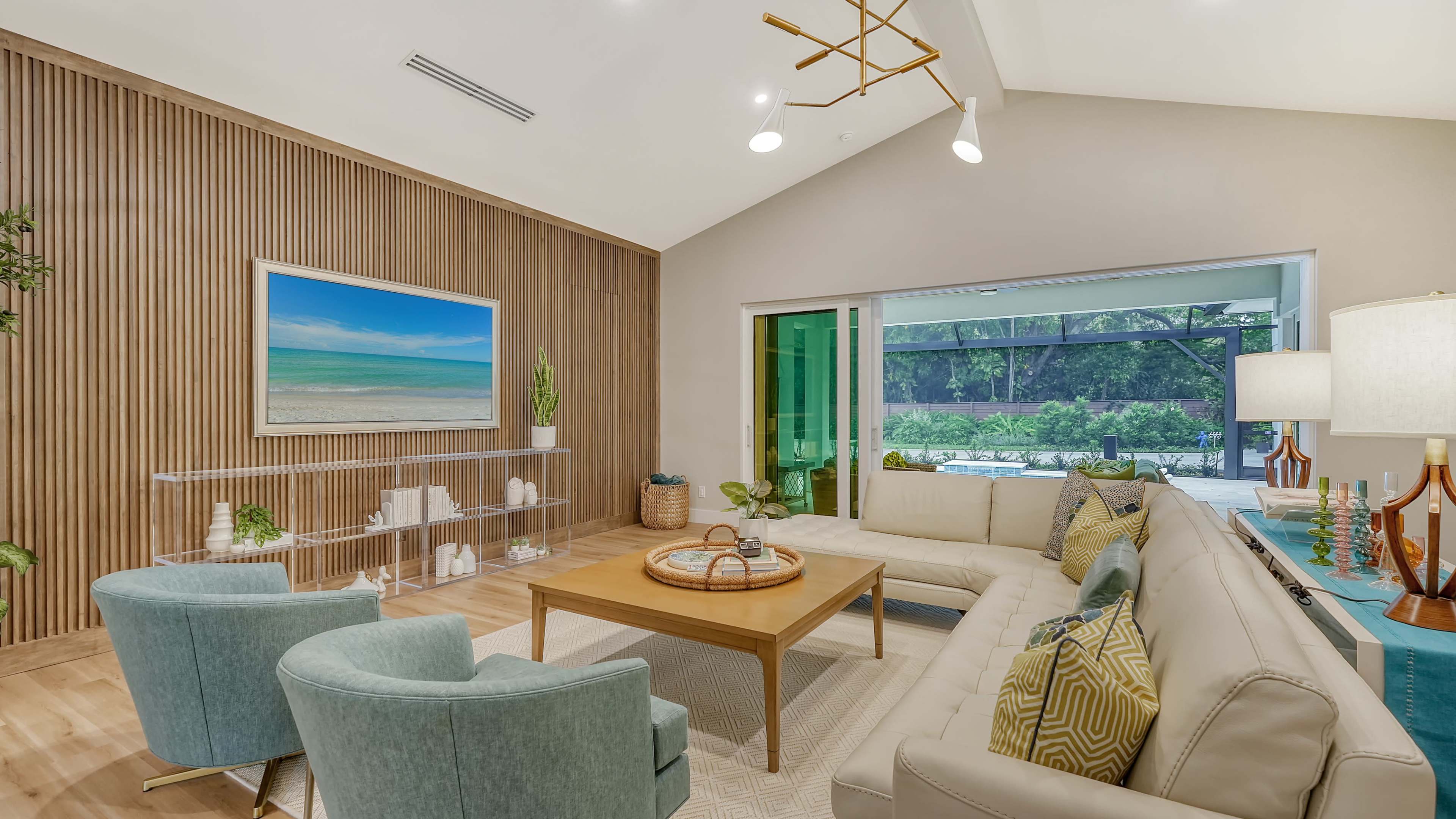 A modern living room features a sectional couch, a wooden accent wall, large windows, and a coffee table adorned with decor.