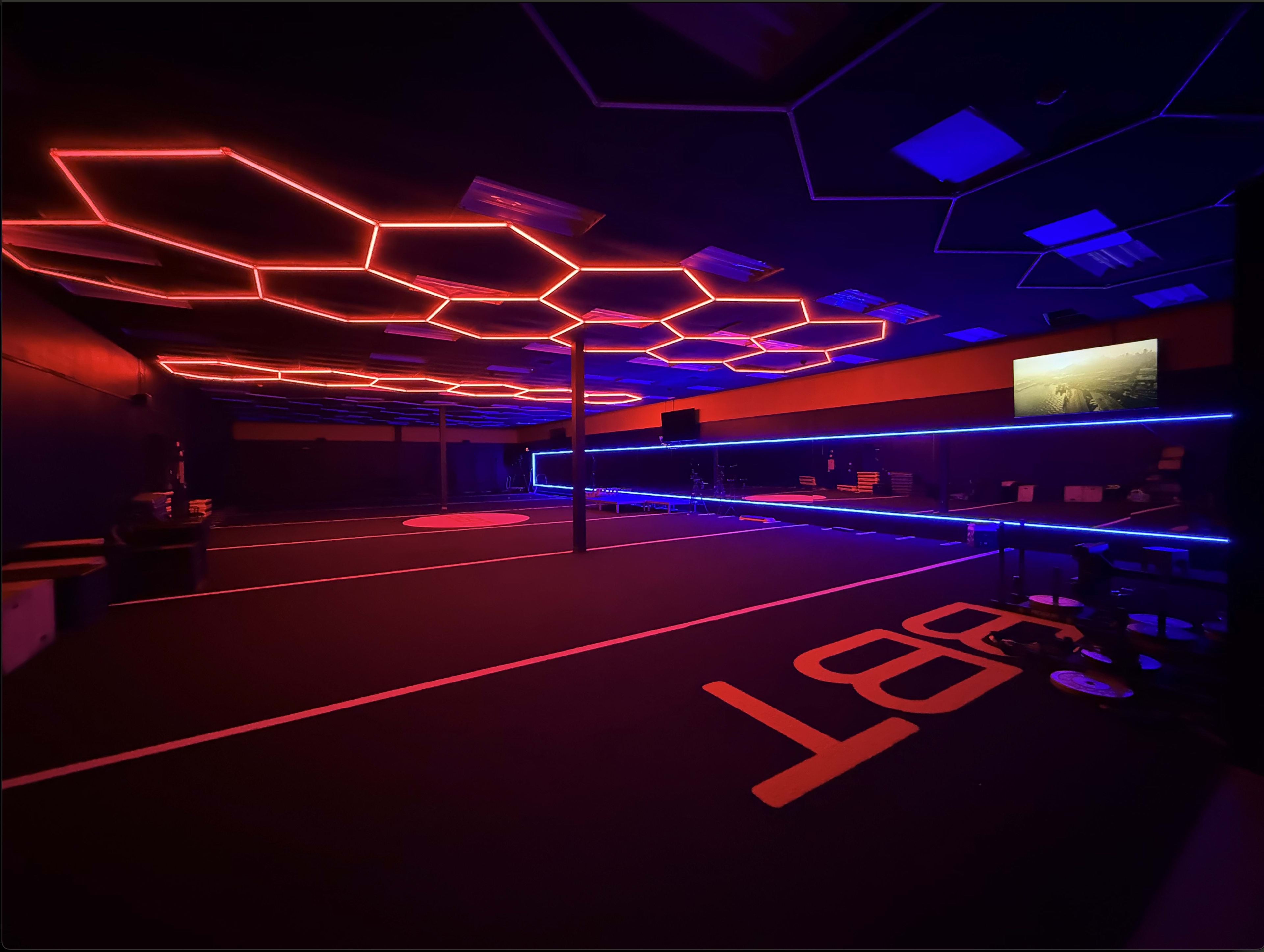 The image shows an indoor space with a dark floor, illuminated by red and blue neon lights arranged in a hexagonal pattern on the ceiling.