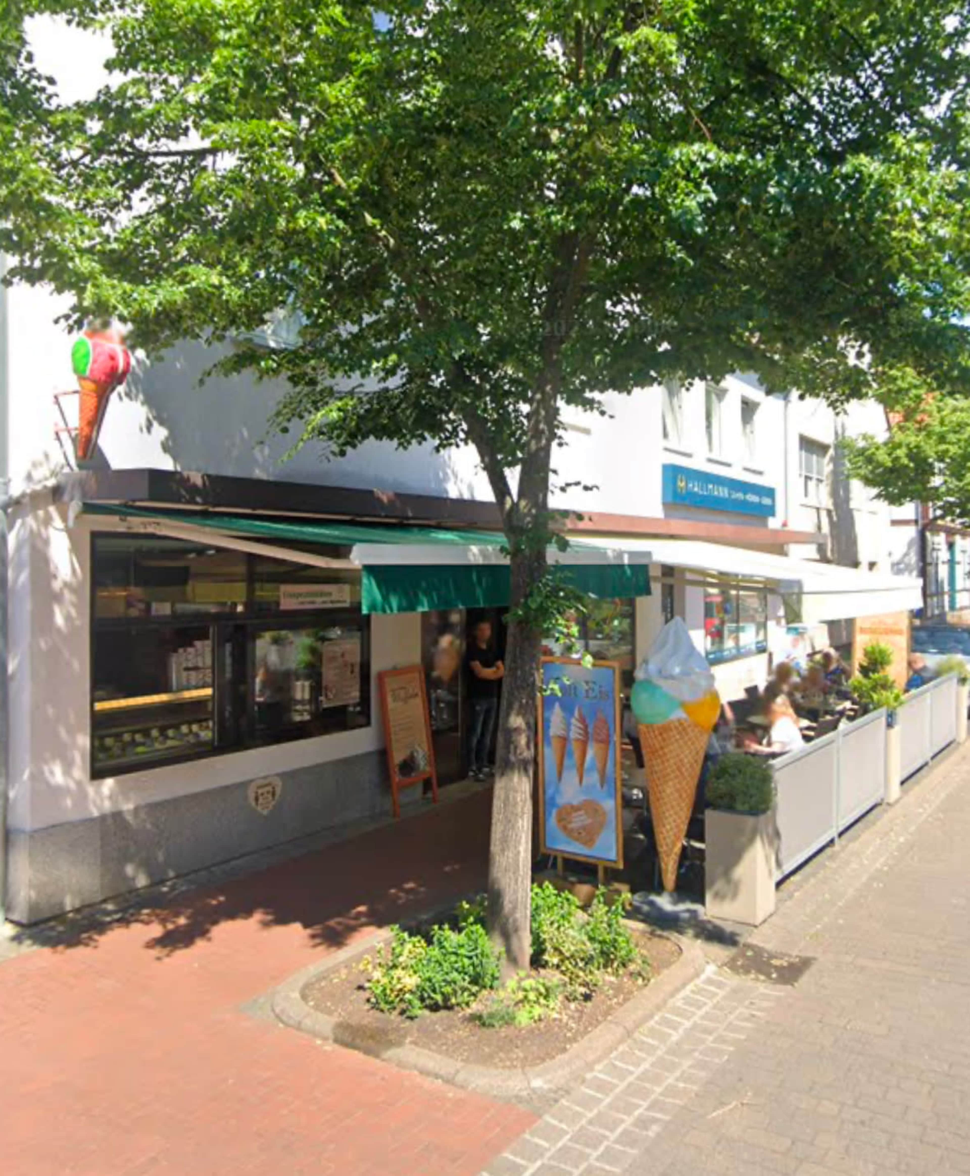 The image shows an ice cream shop with a green awning, outdoor seating, and large ice cream cone displays in front.