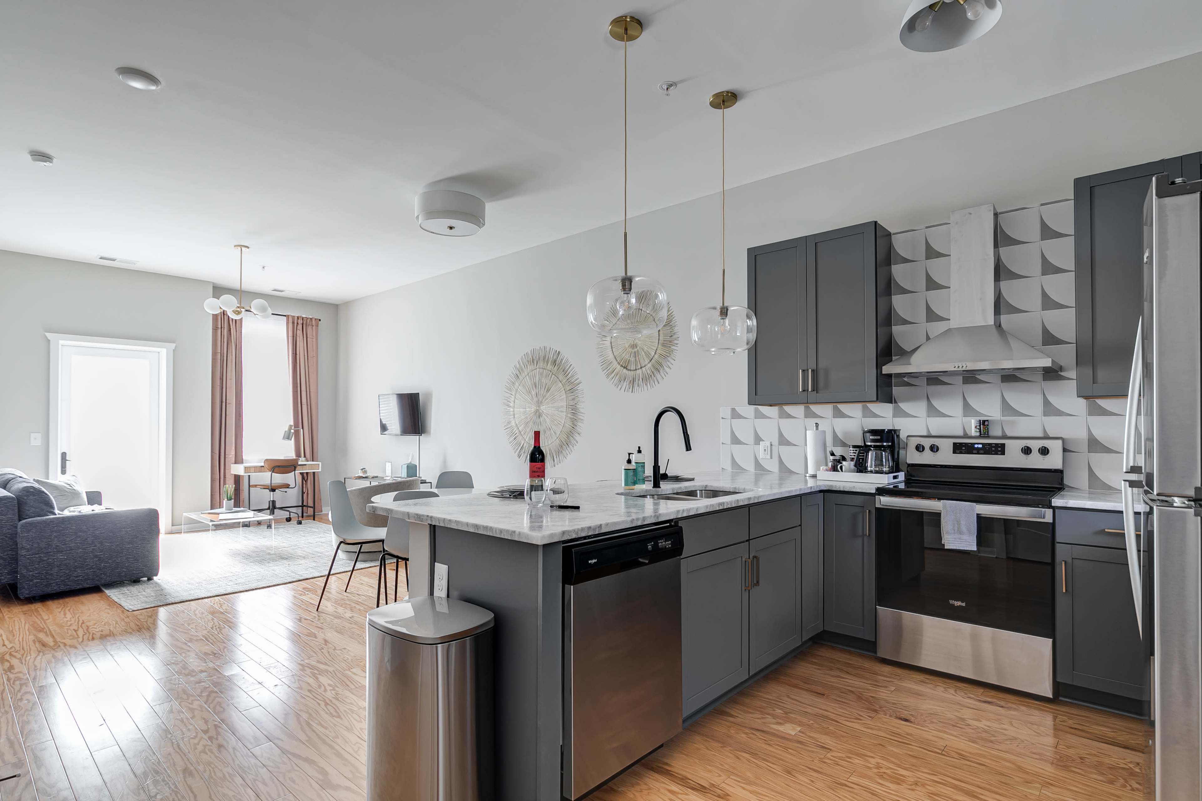 A modern kitchen with gray cabinets, a marble countertop, stainless steel appliances, and a dining area with a table and chairs.