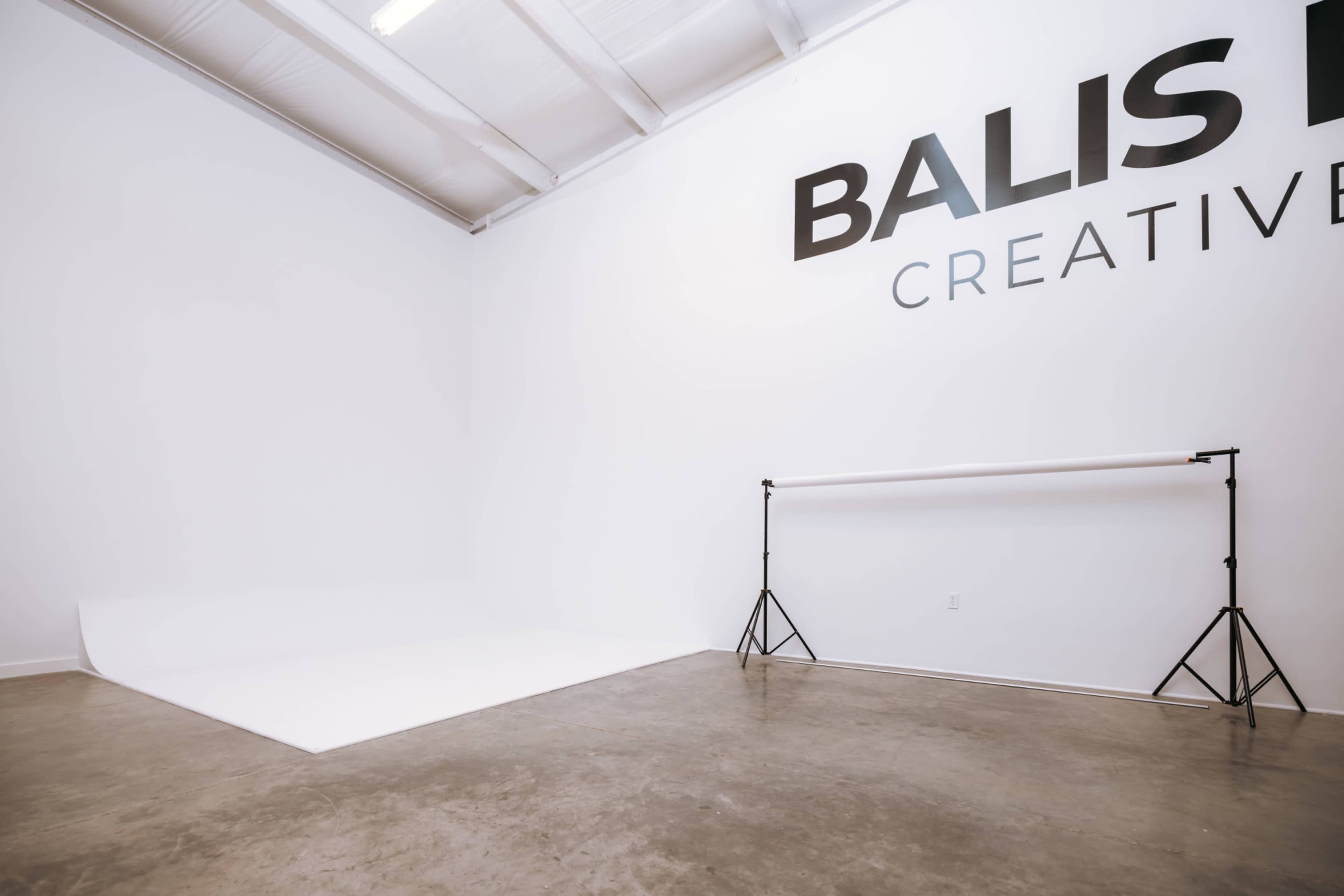 The image shows a spacious photography studio with a plain white backdrop and the words "BALIS B CREATIVE" displayed on the wall.