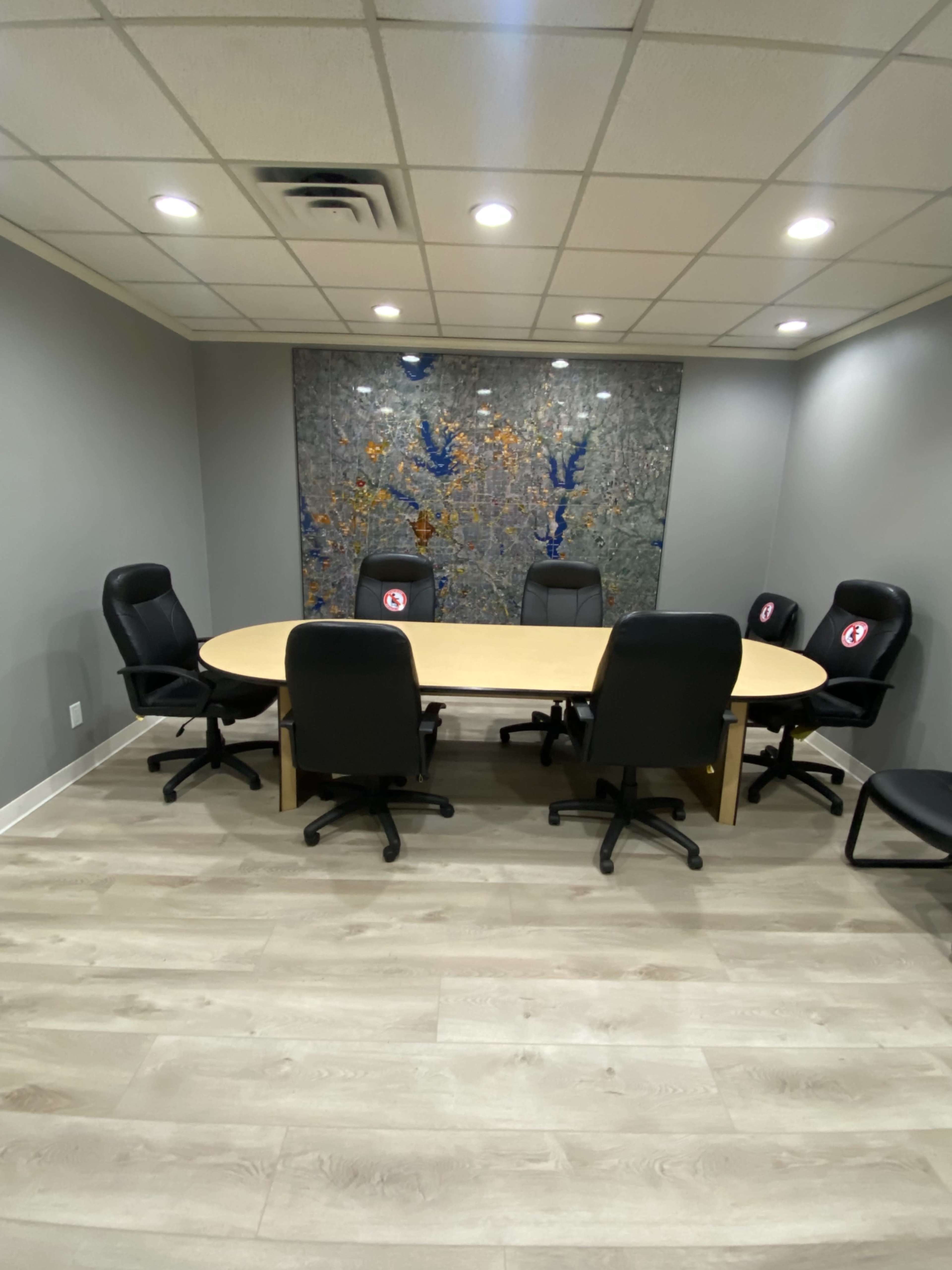 A conference room with a large oval table surrounded by black office chairs and a decorative wall in the background.
