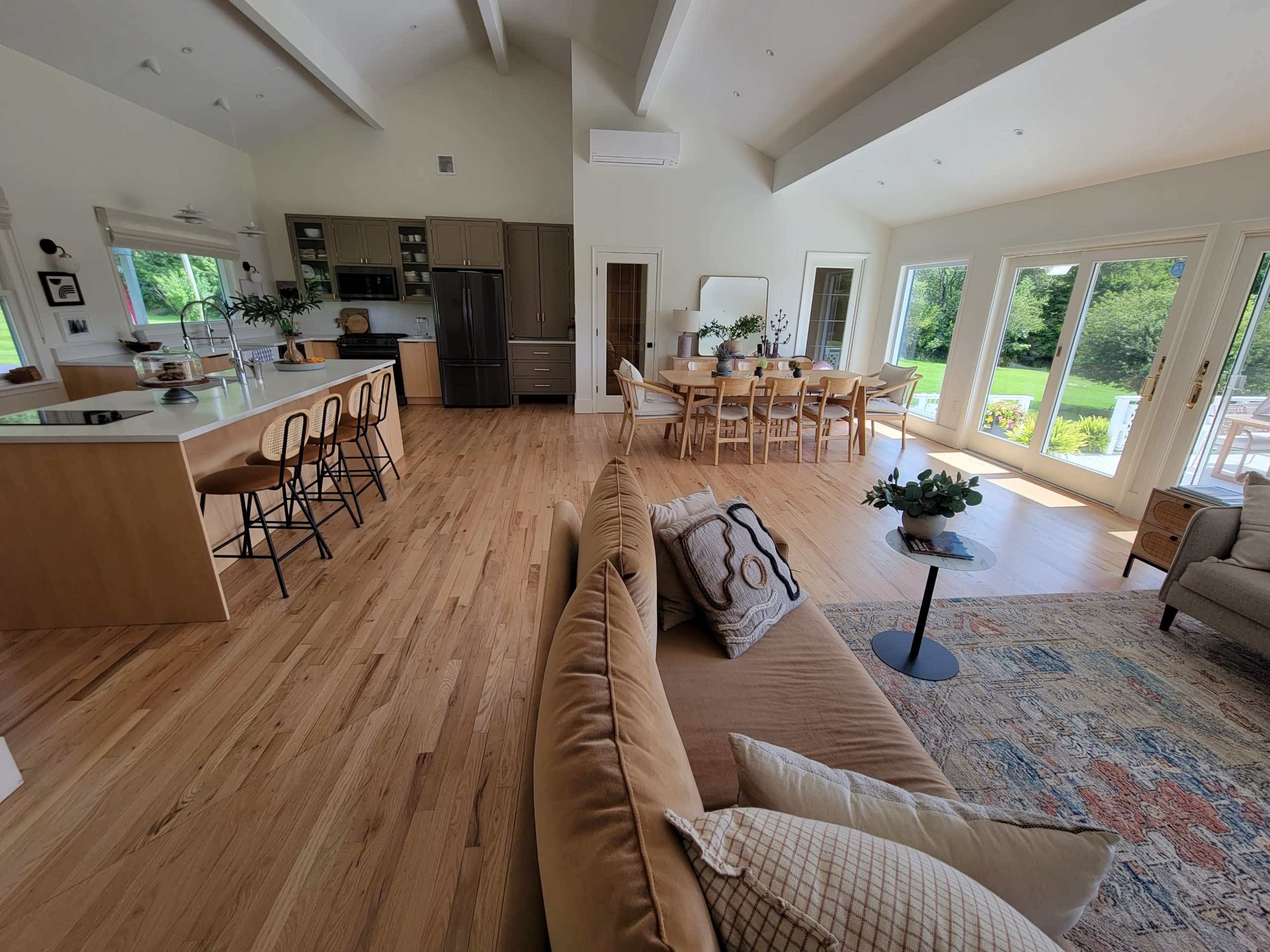 An open-concept living space featuring a modern kitchen on one side and a dining area with large windows overlooking a garden on the other.