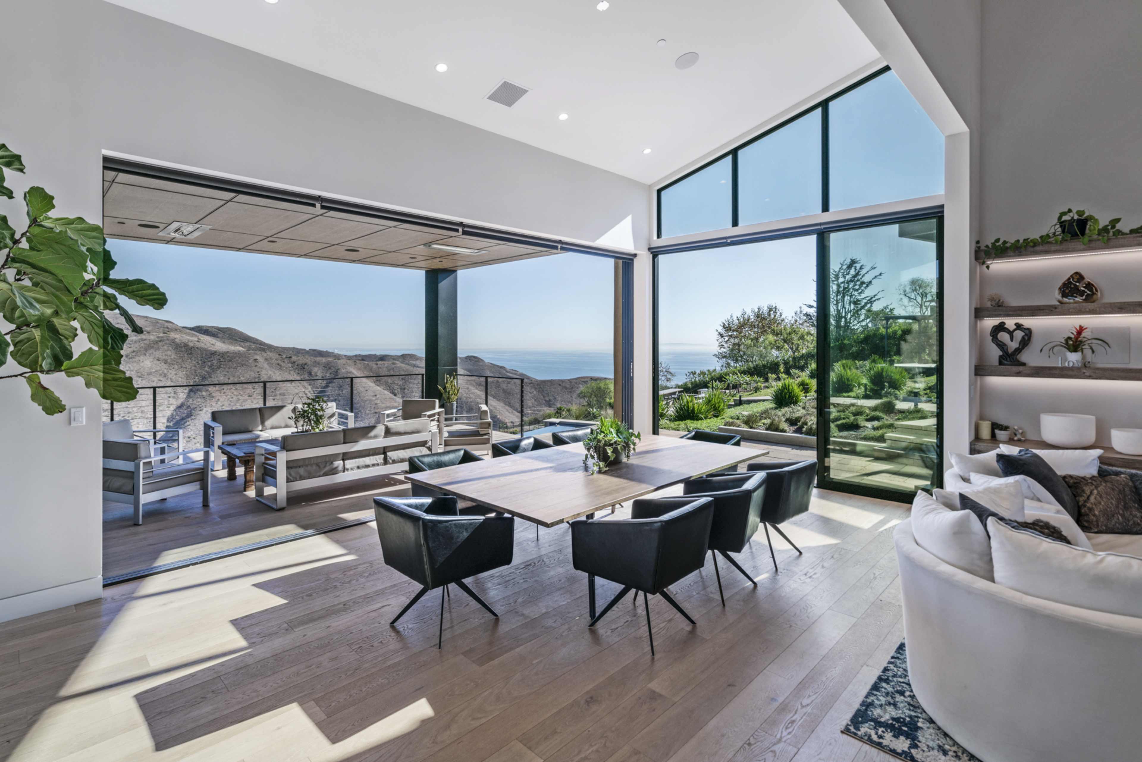 A modern dining area with large windows overlooking a scenic view of hills and a body of water.