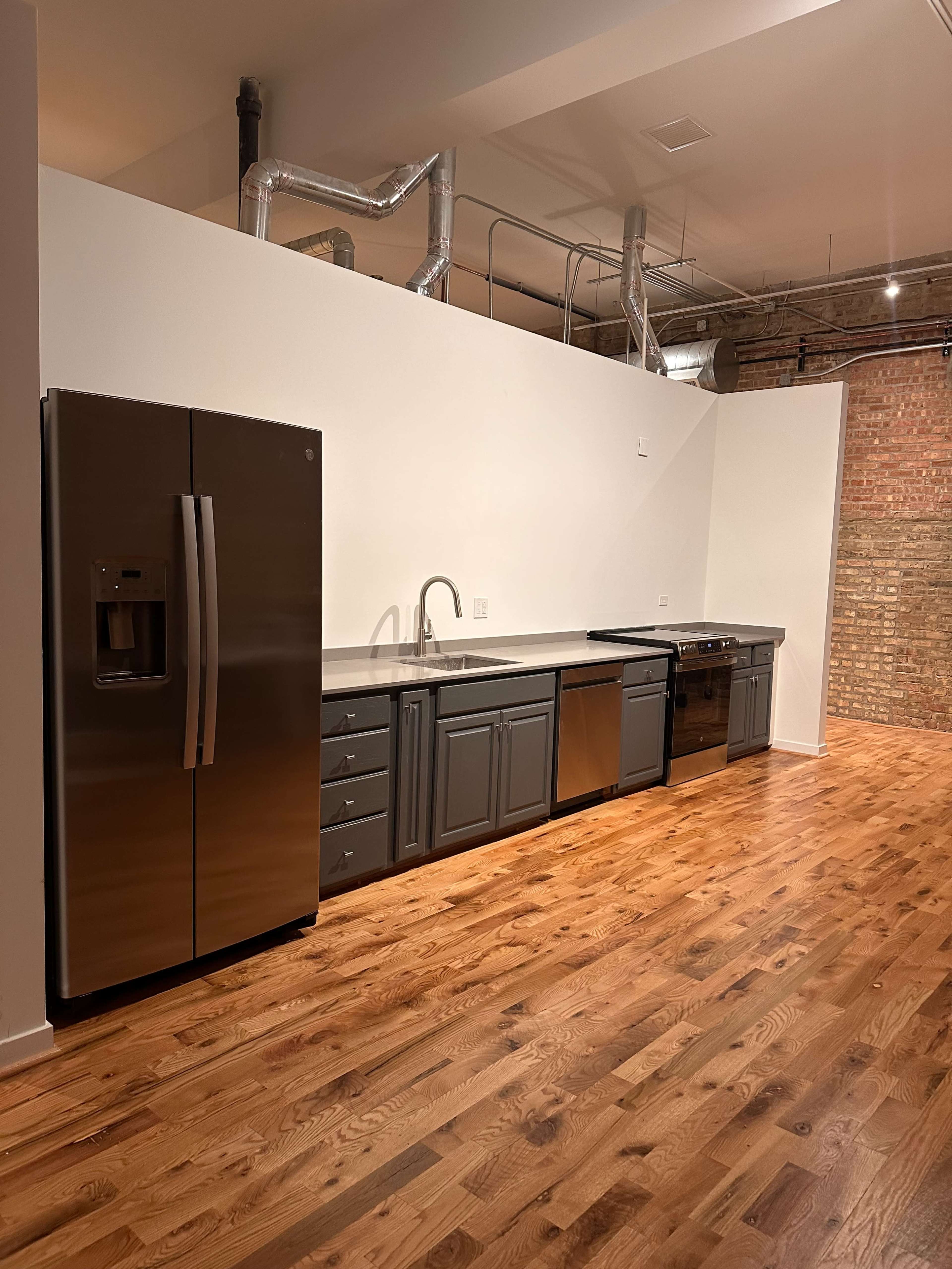 The image shows a modern kitchen featuring stainless steel appliances, dark cabinetry, and hardwood flooring.