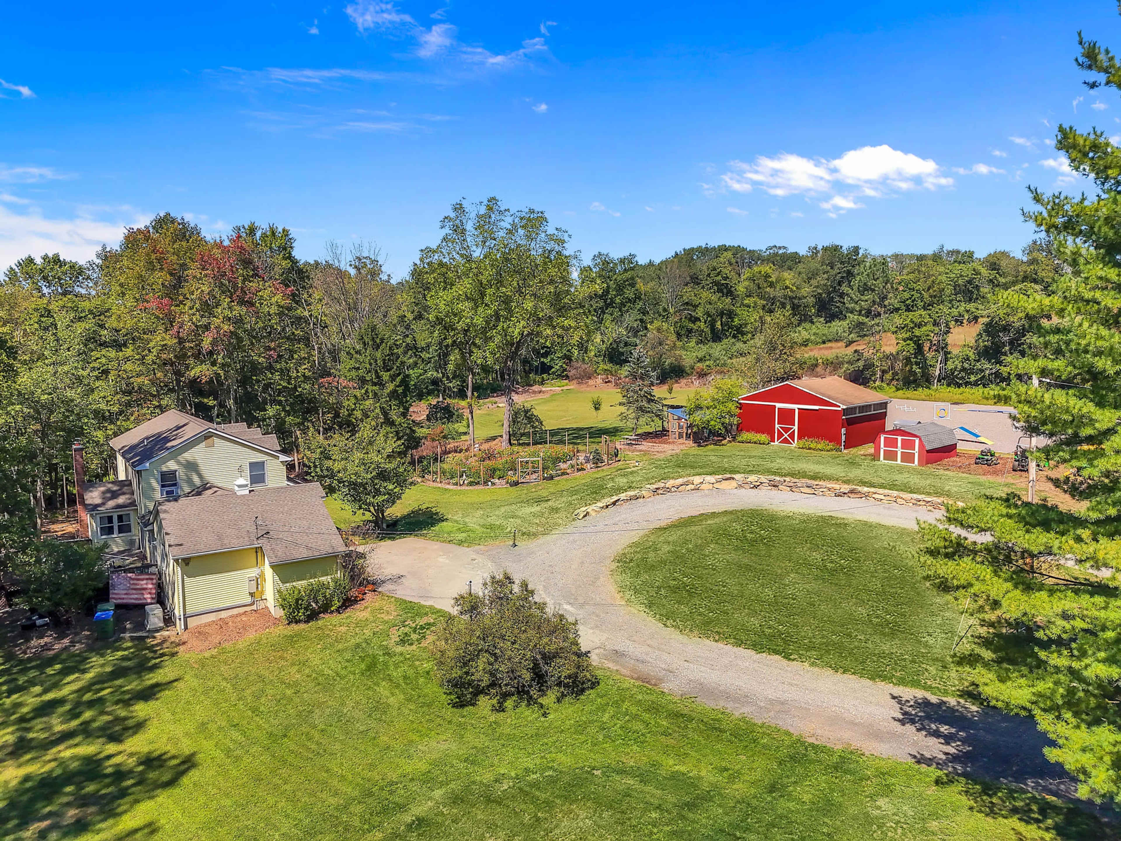 The image shows a rural property featuring a house, a red barn, and an open grassy area surrounded by trees and fields.