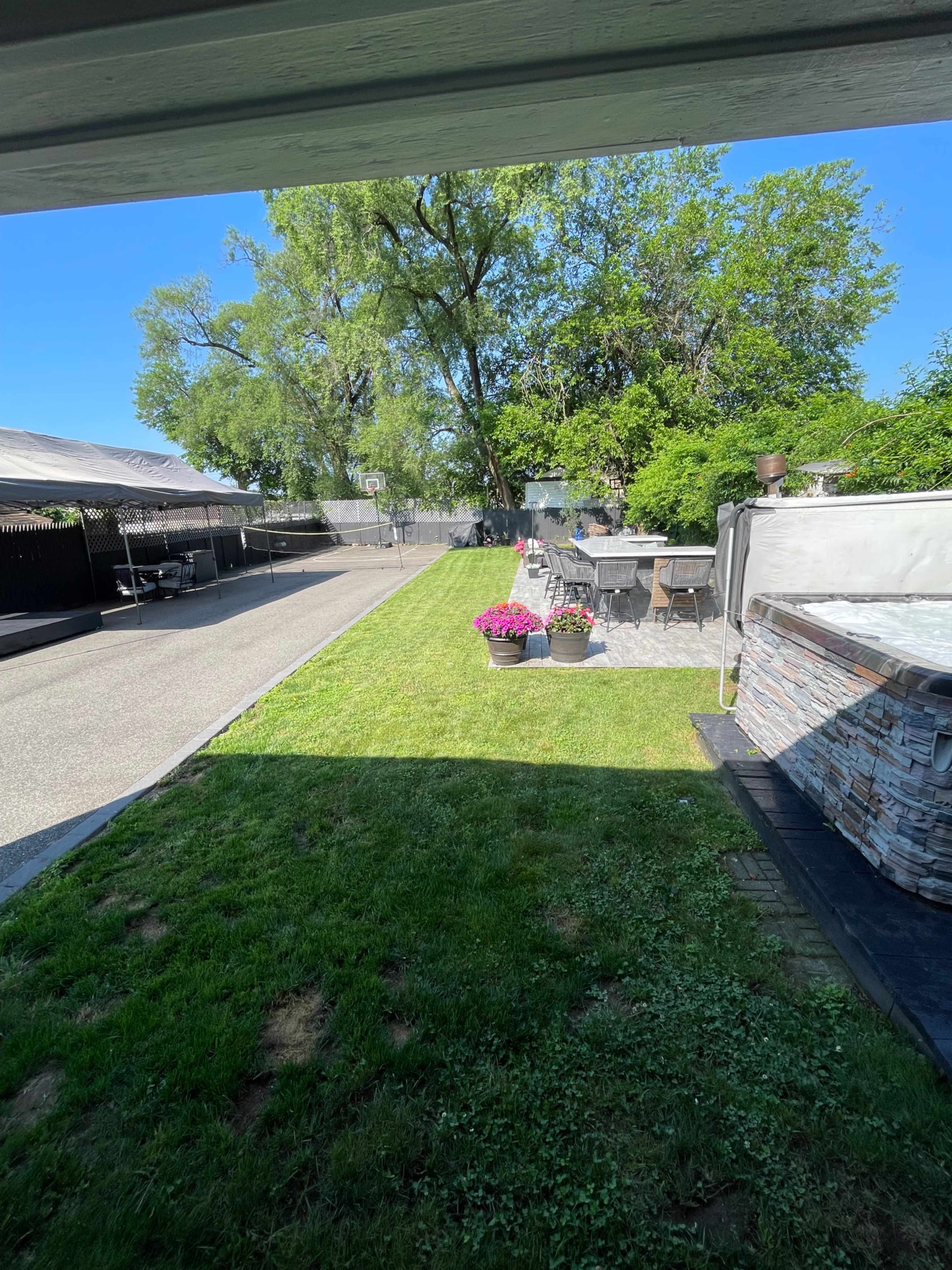 The image shows a backyard scene with a neatly maintained lawn, planters with flowers, and a patio area with outdoor furniture.