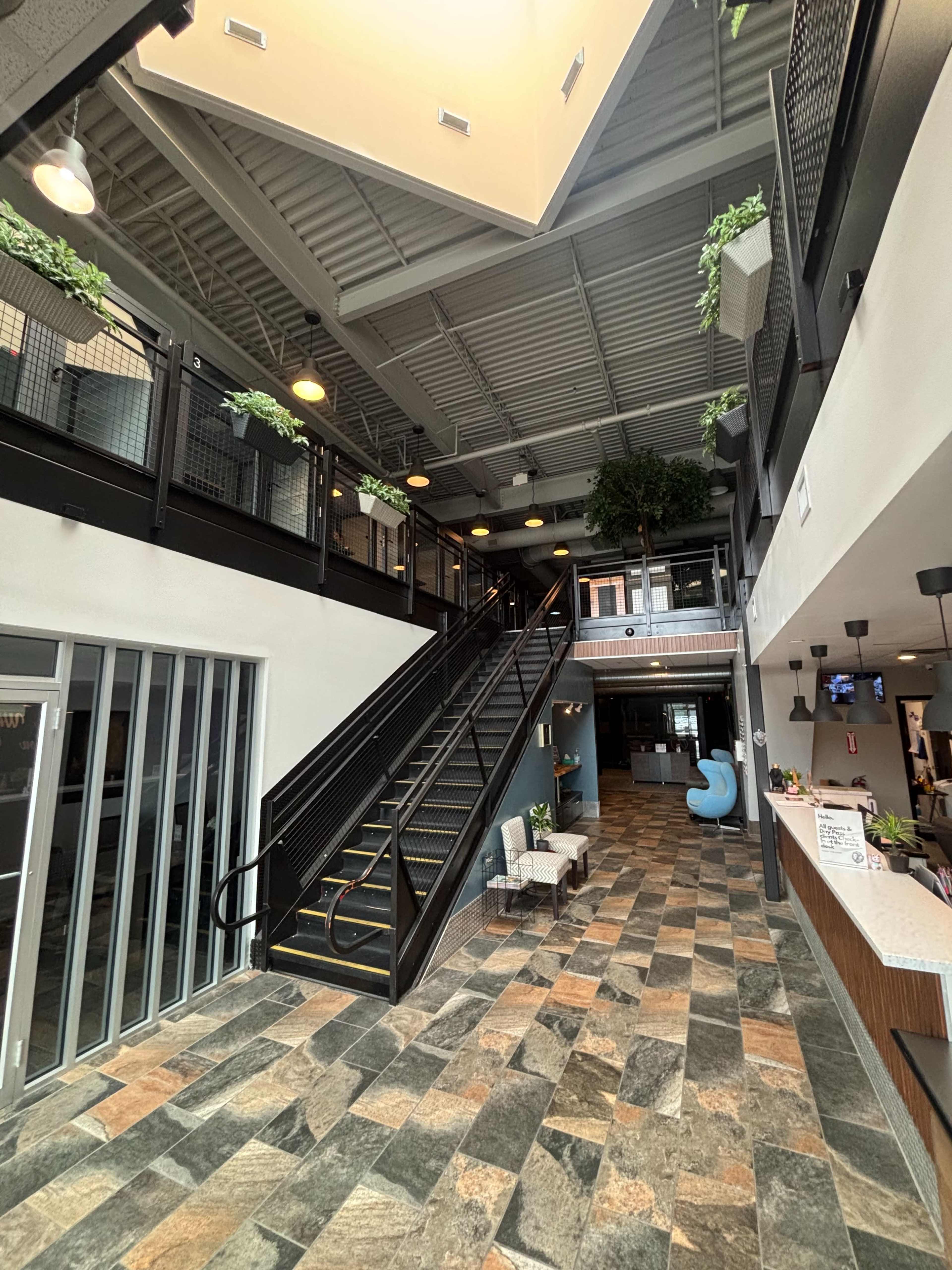 The image shows a spacious entrance area featuring a prominent staircase, a tile floor with varied patterns, and large windows allowing natural light to fill the space.