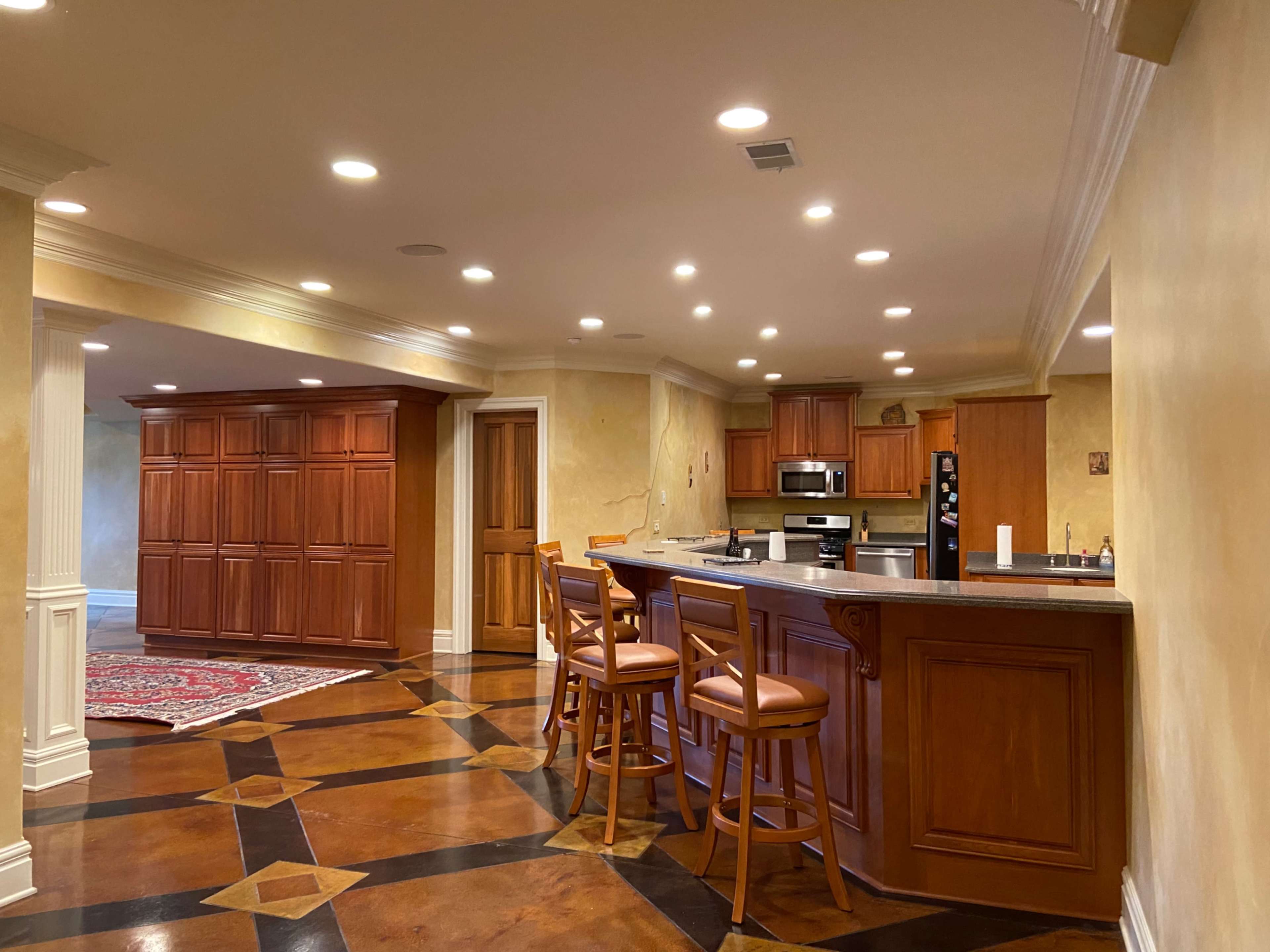 A spacious, modern kitchen with wooden cabinetry, a large central island, and a polished floor featuring geometric patterns.