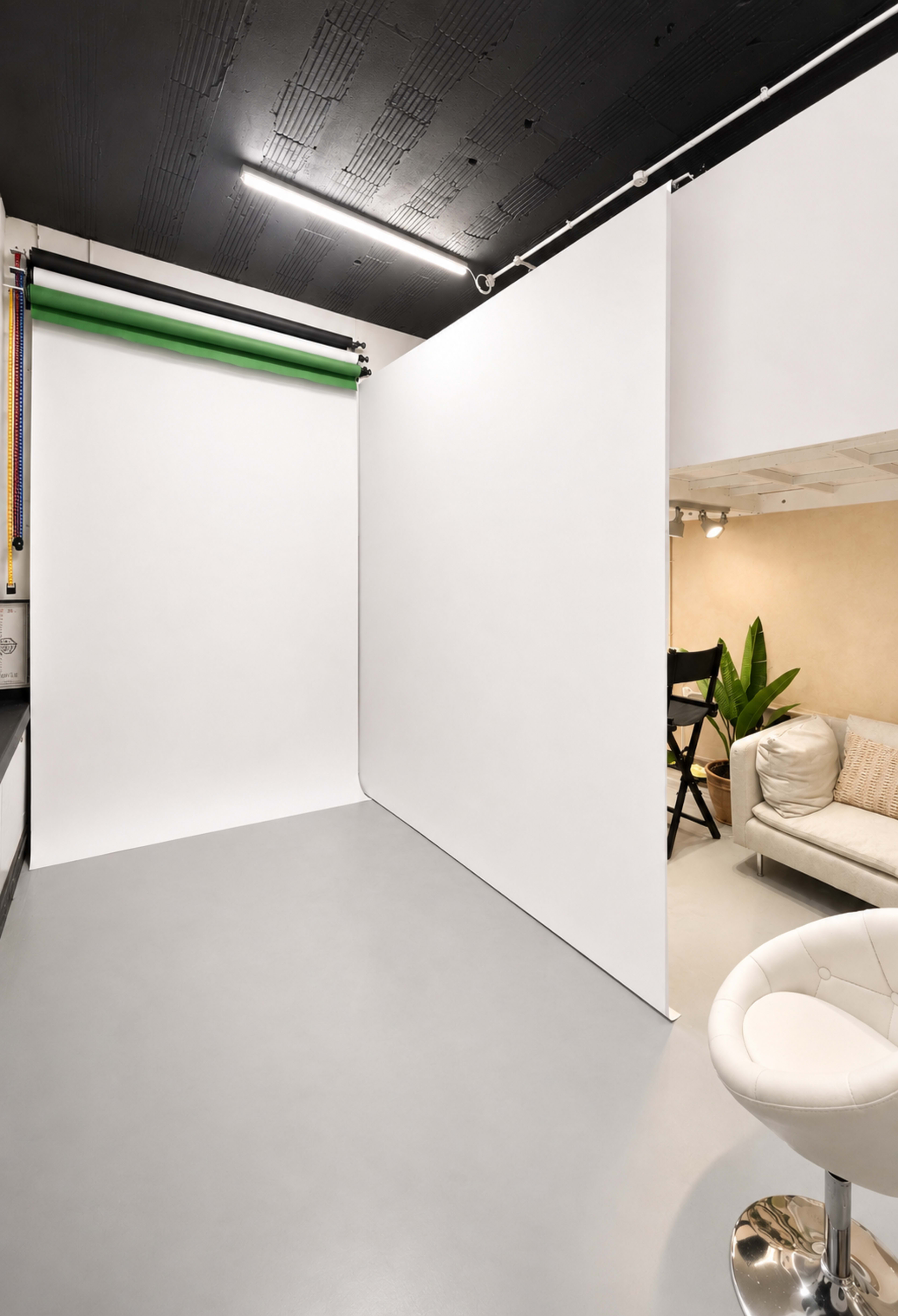 The image shows a photography studio featuring a large white backdrop, a green gradient roll-up background, and minimalist furnishings, including a light-colored couch and a stool.