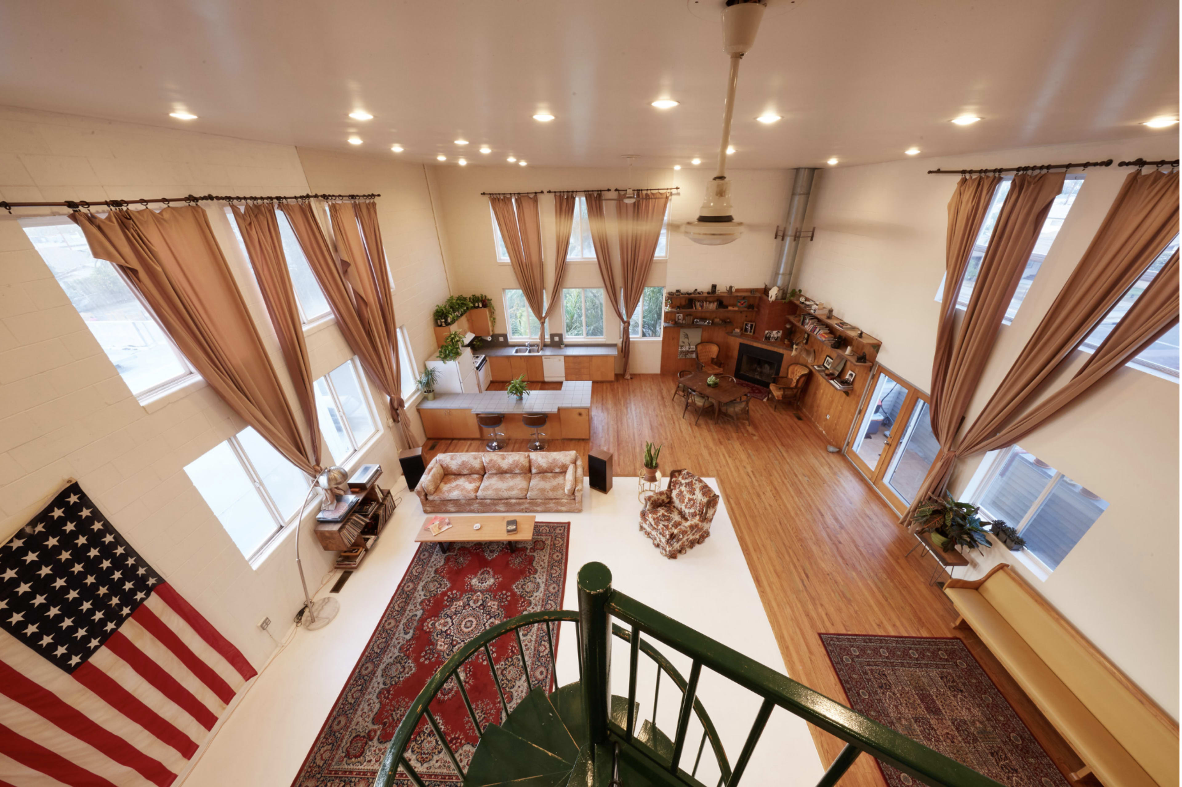 A spacious, well-lit living room with large windows, a spiral staircase, and an American flag hanging on one wall.