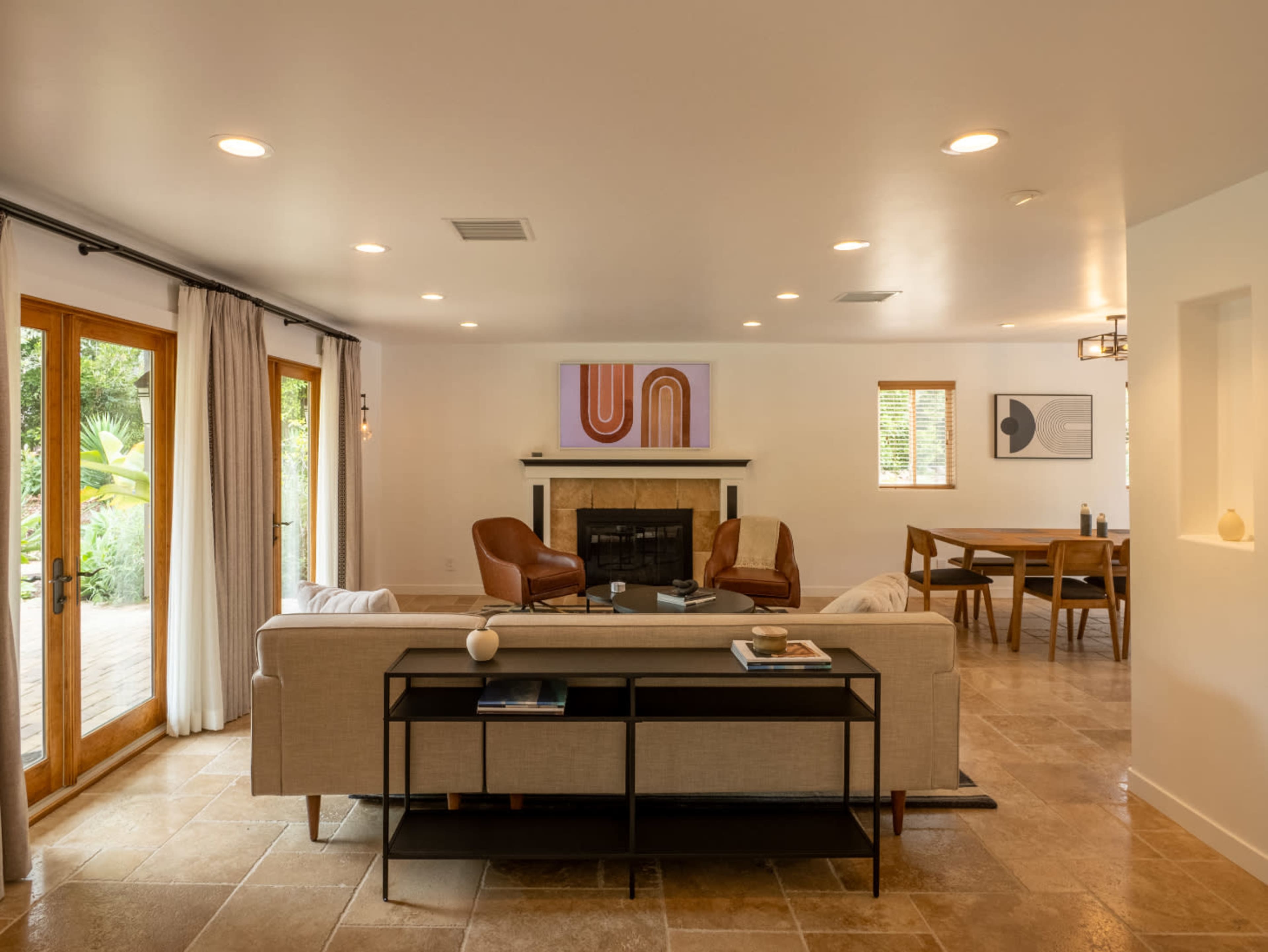 A spacious living room featuring a beige sofa, two brown chairs, a fireplace, and a dining area with a wooden table in the background.