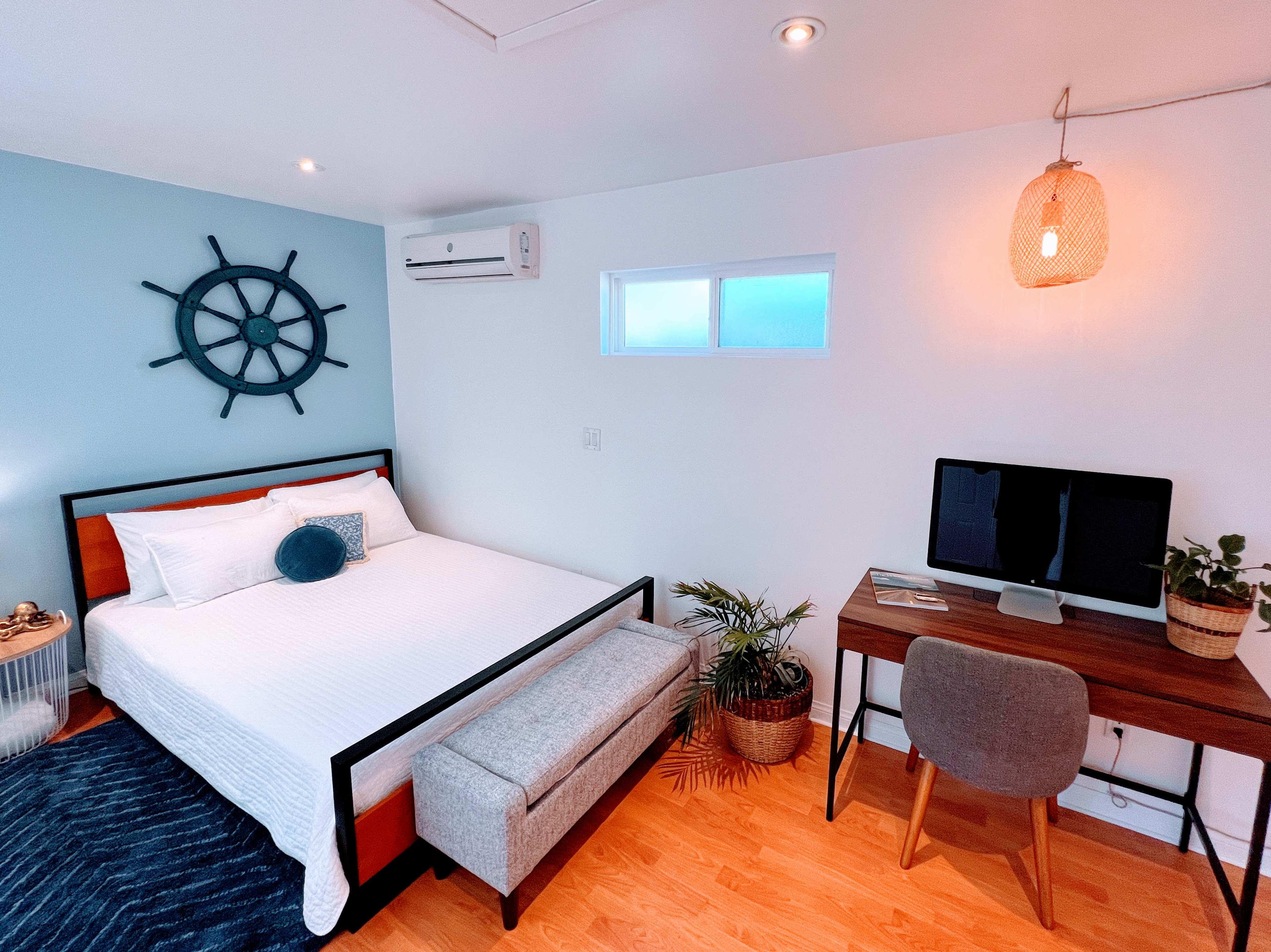 A modern bedroom featuring a bed, a desk with a computer, and a decorative ship's wheel on the wall.