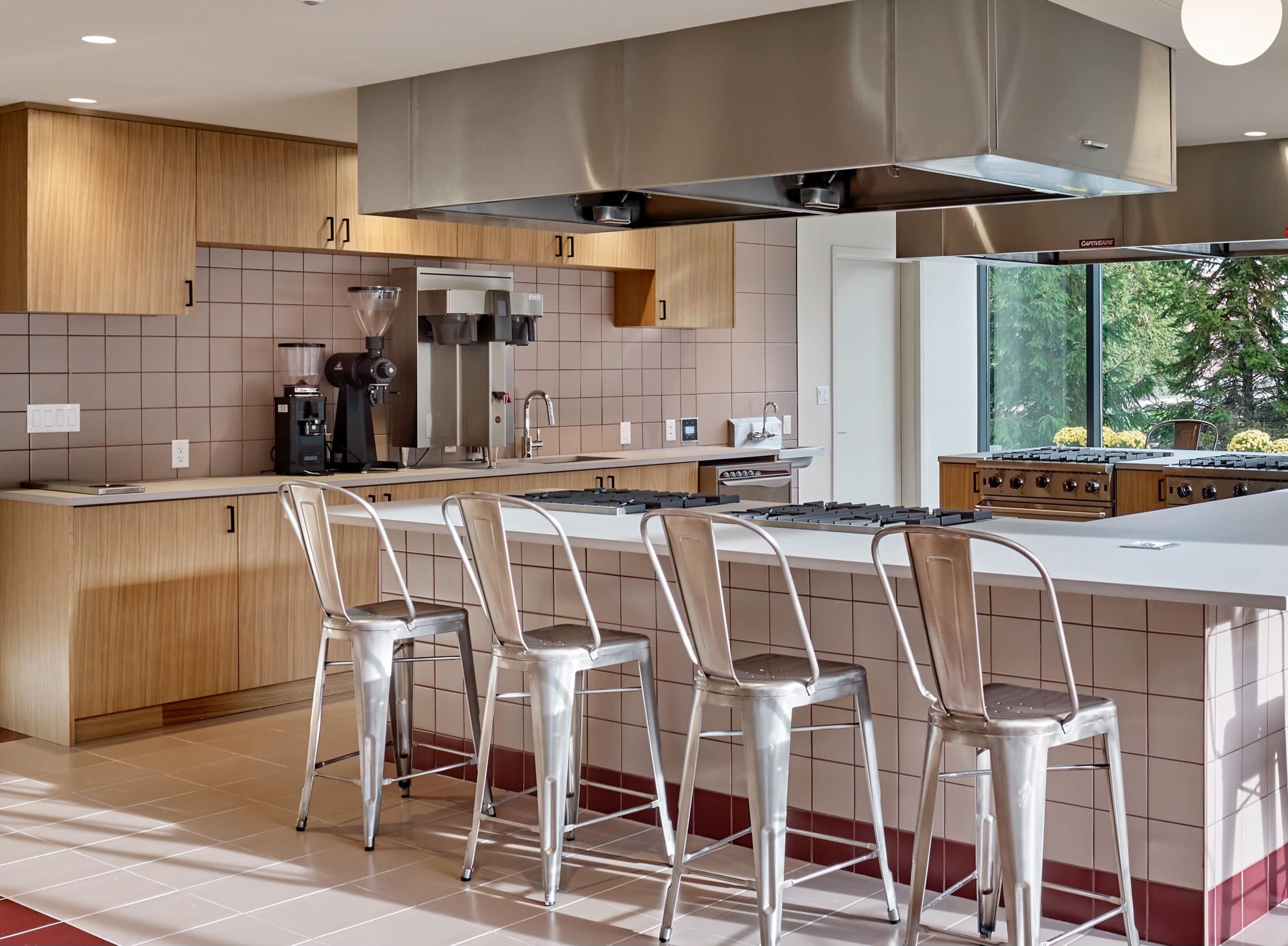 A modern kitchen with wooden cabinetry, a large island with barstool seating, and a stainless steel exhaust hood.