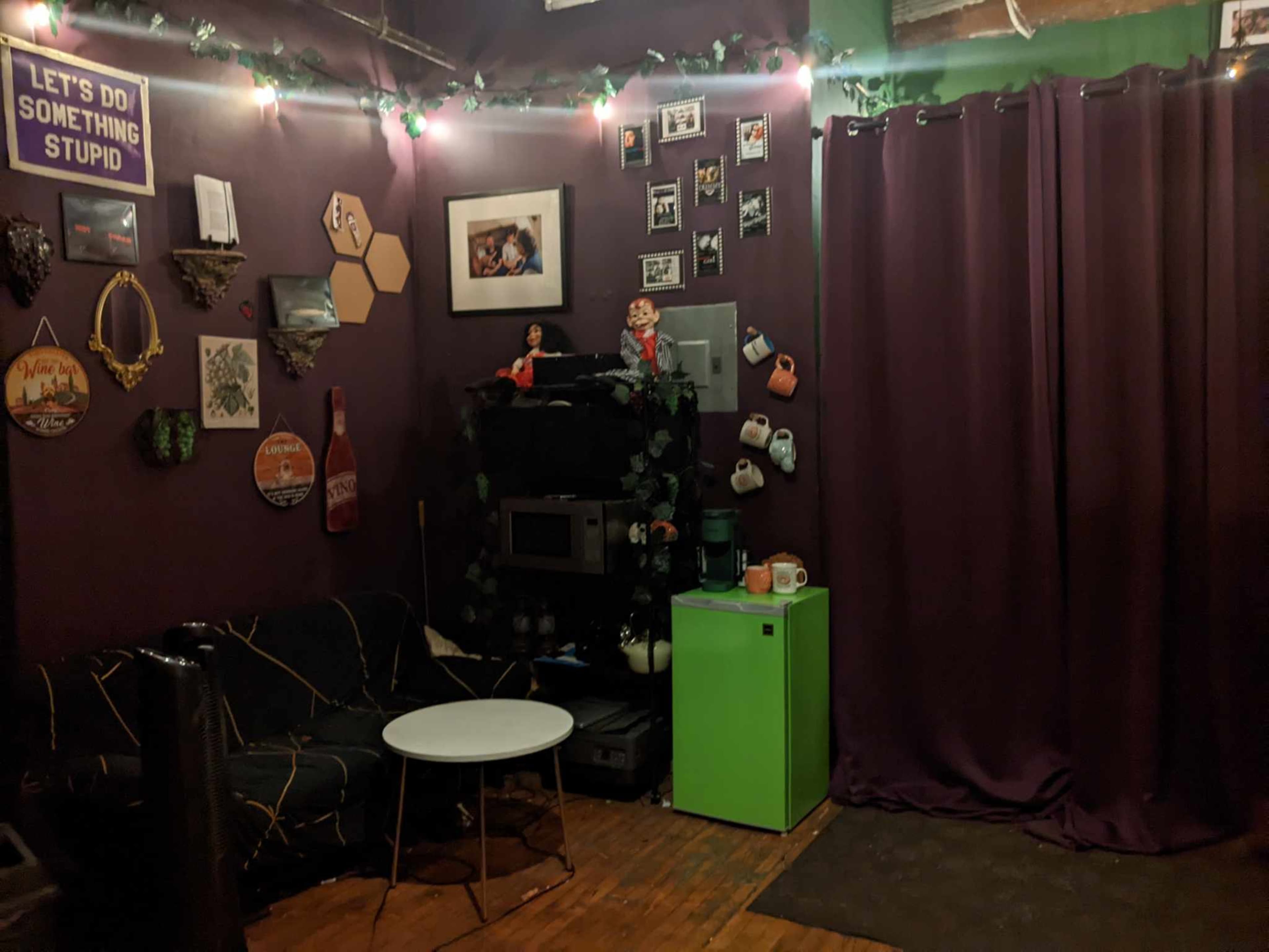 A cozy room with purple walls, a green mini fridge, a coffee table, and various decorations including photos and wall art.