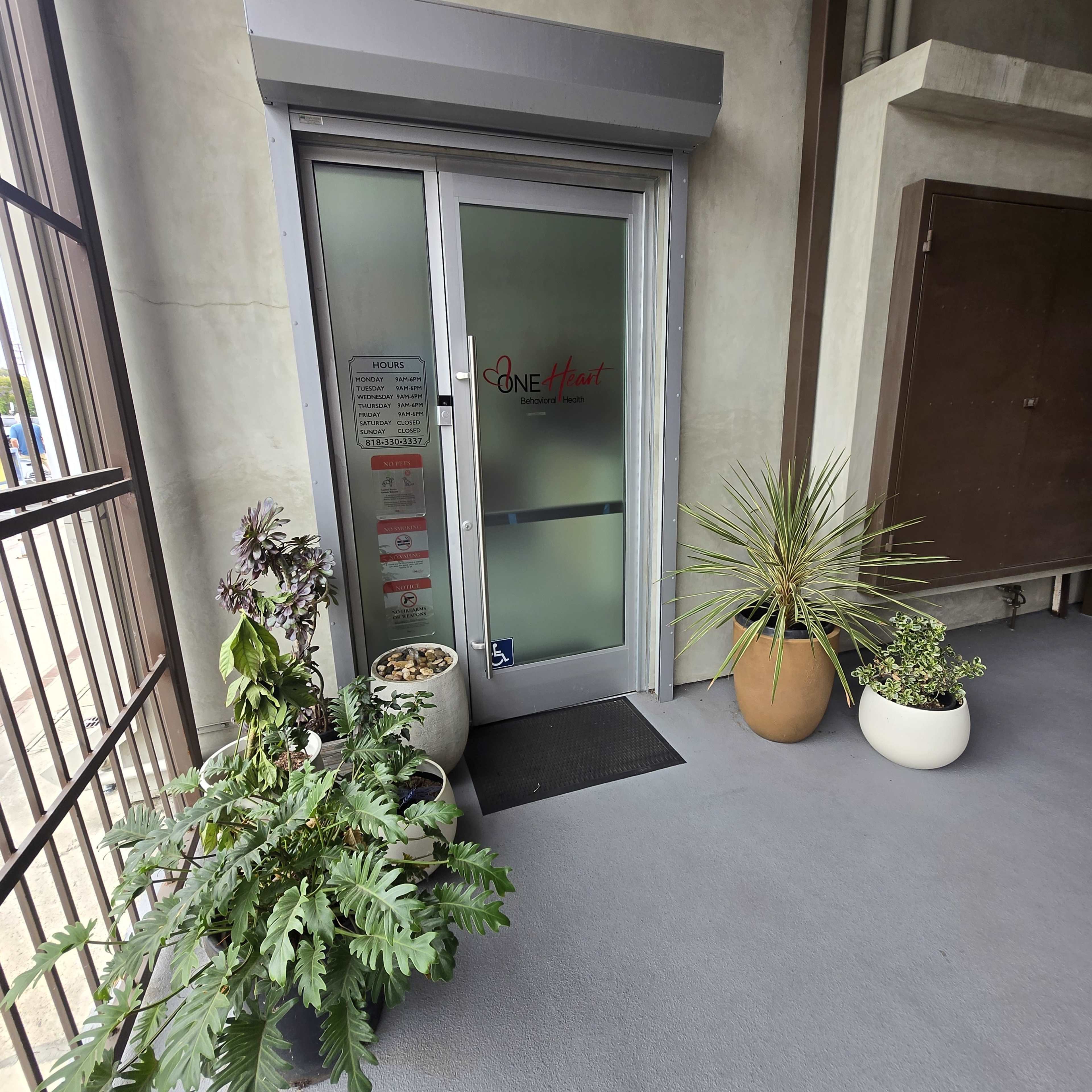 The image shows a building entrance with a glass door displaying the name "Cone Heart" and surrounded by potted plants.