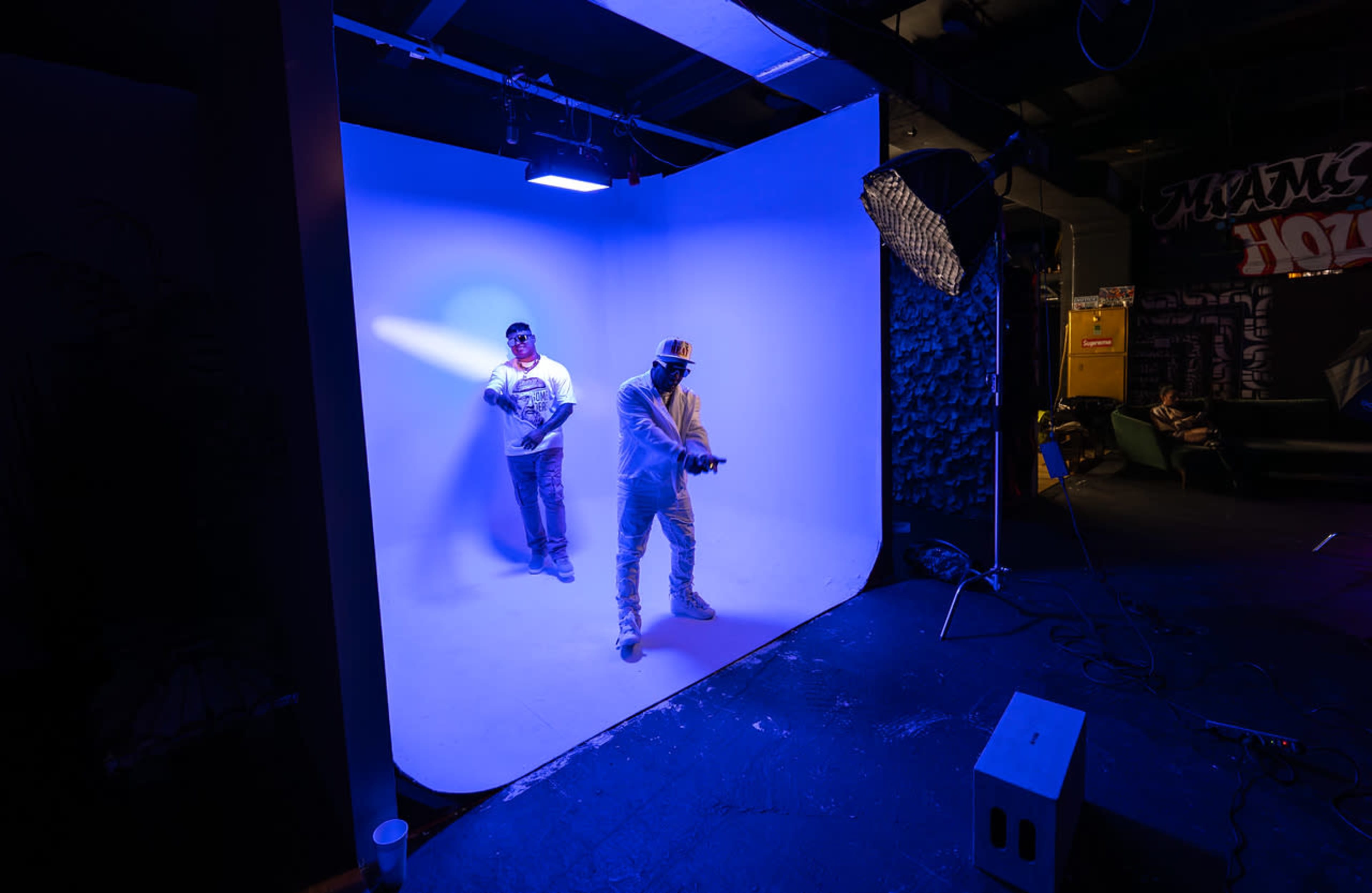 Two individuals pose in front of a blue backdrop in a photography studio.