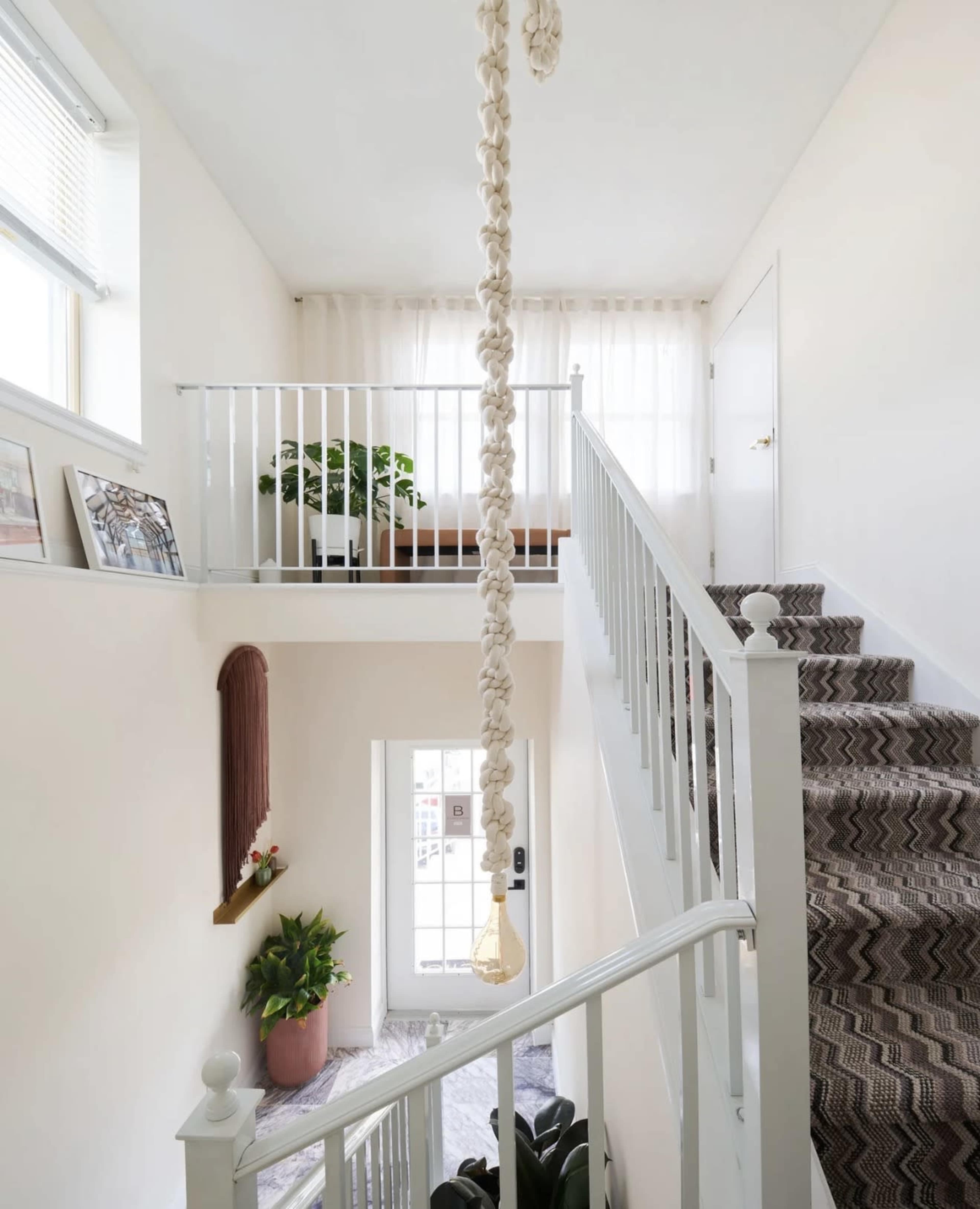 The image shows a well-lit staircase with a decorative rope hanging from the ceiling and a small seating area visible near a window at the top.