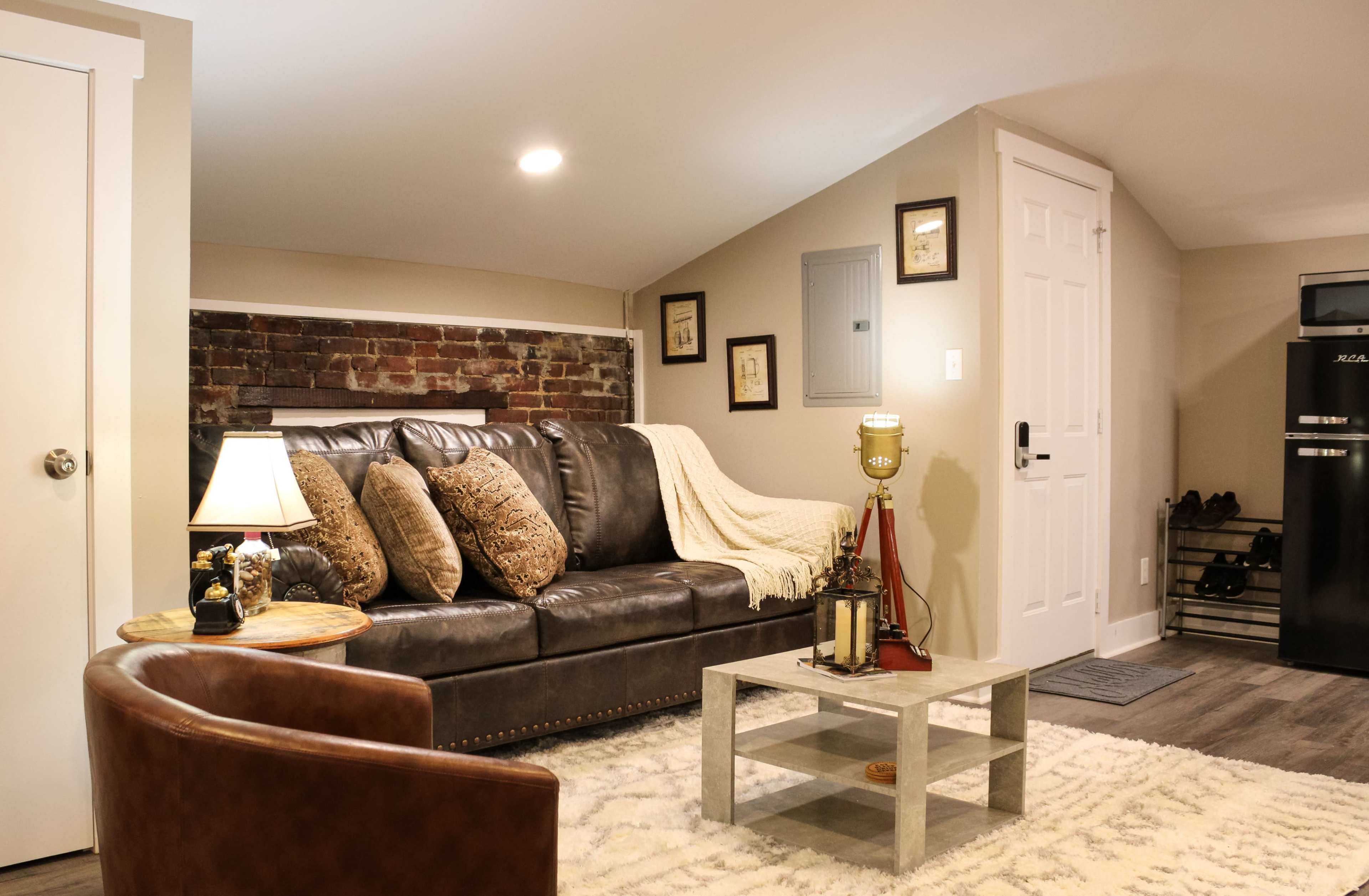 A cozy living room with a brown leather sofa, a small coffee table, a lamp, and exposed brick walls.