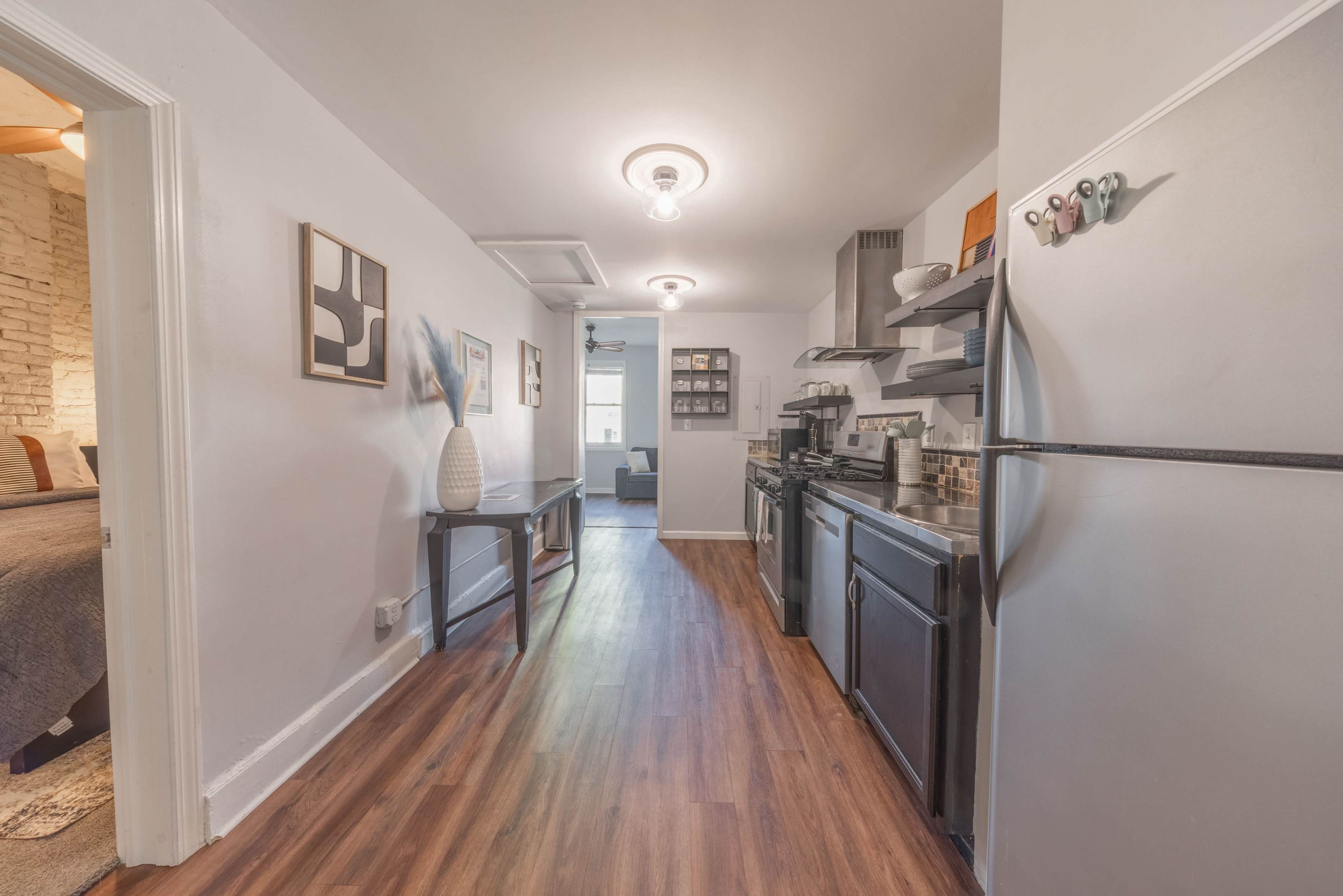 A narrow hallway leads from a kitchen with a stainless steel refrigerator to a living area visible at the end.