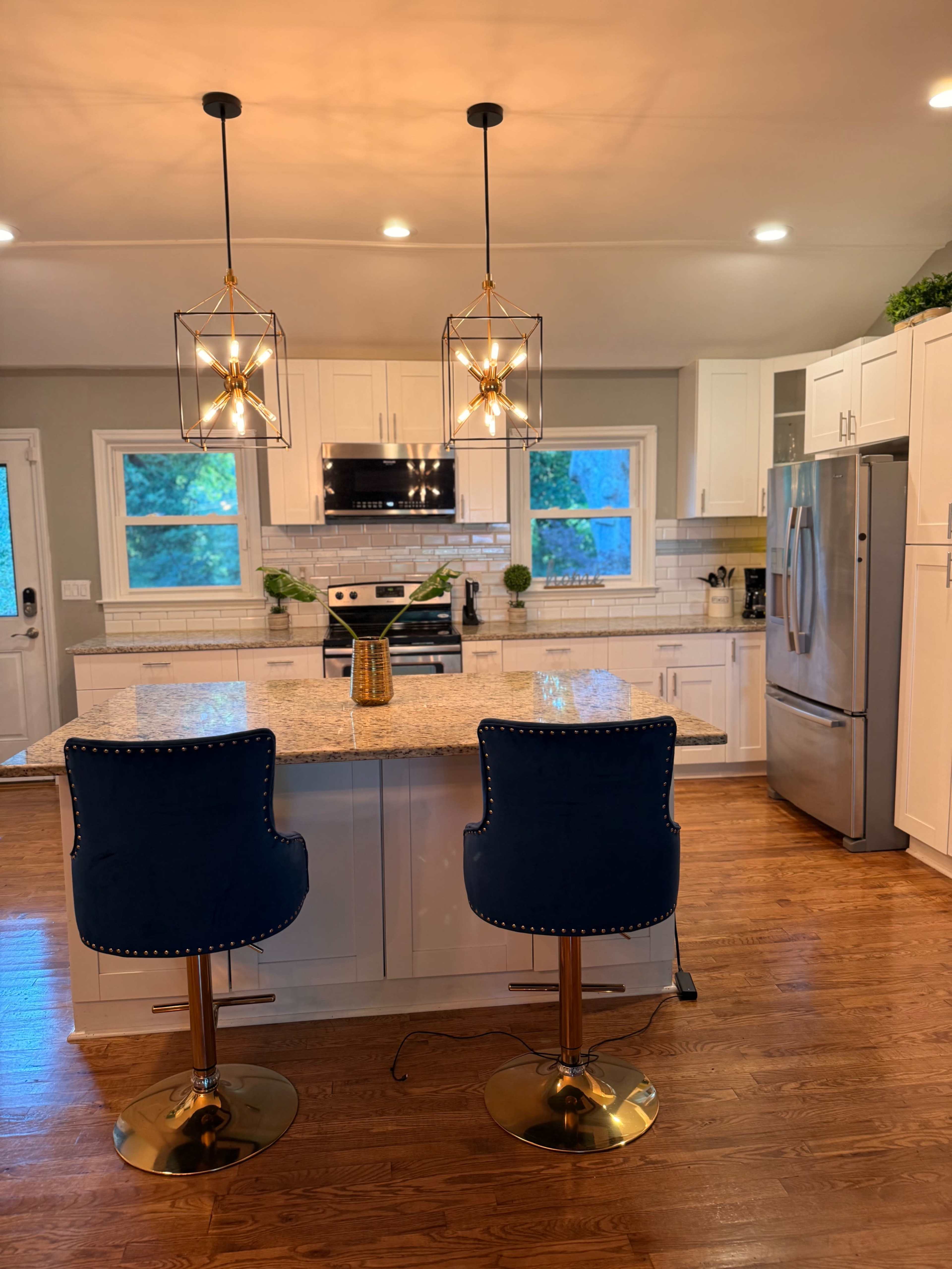A modern kitchen features white cabinetry, granite countertops, two blue bar stools, and pendant lighting above the island.