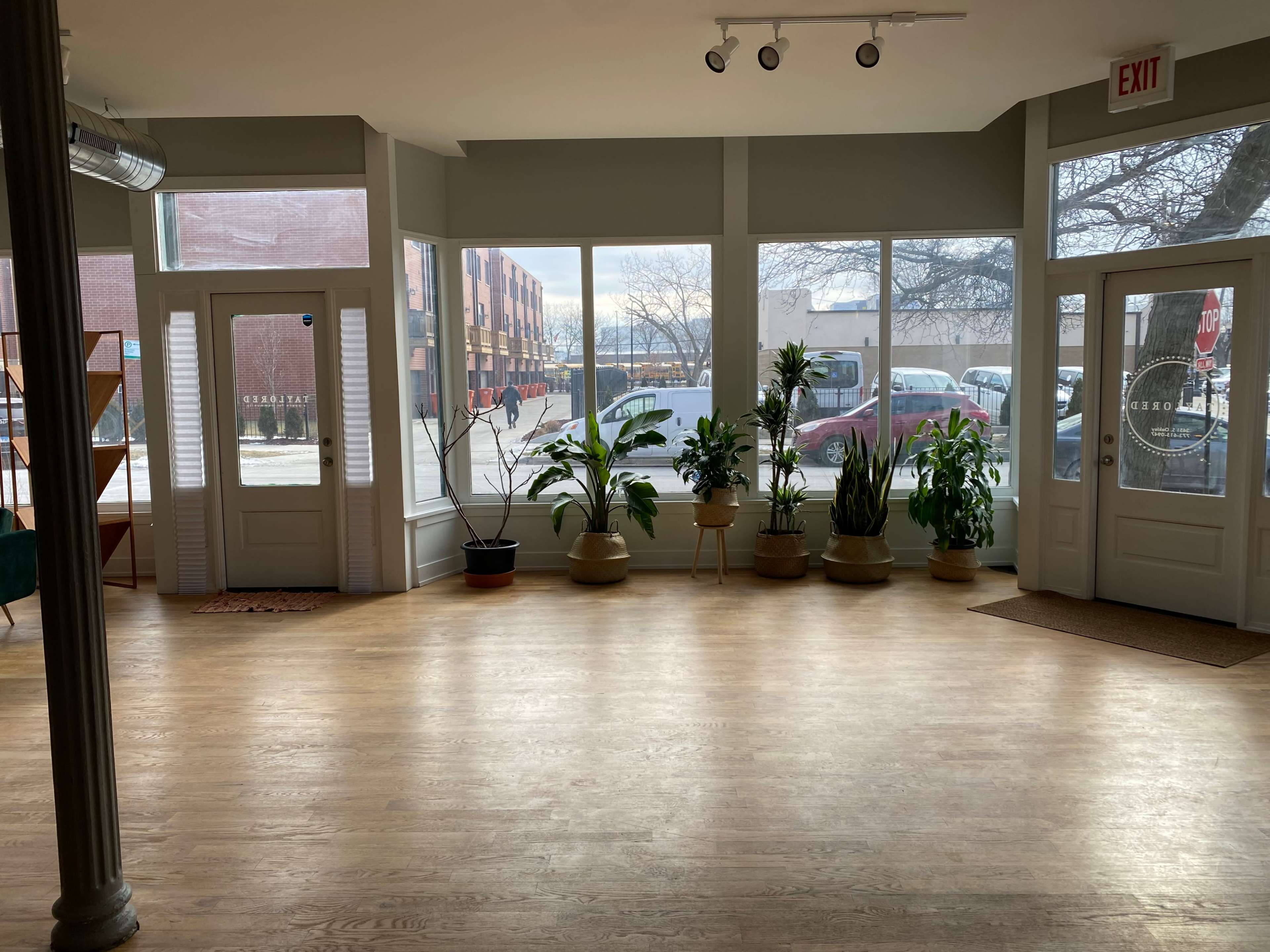 A well-lit room with large windows displaying several potted plants and two doors leading outside.