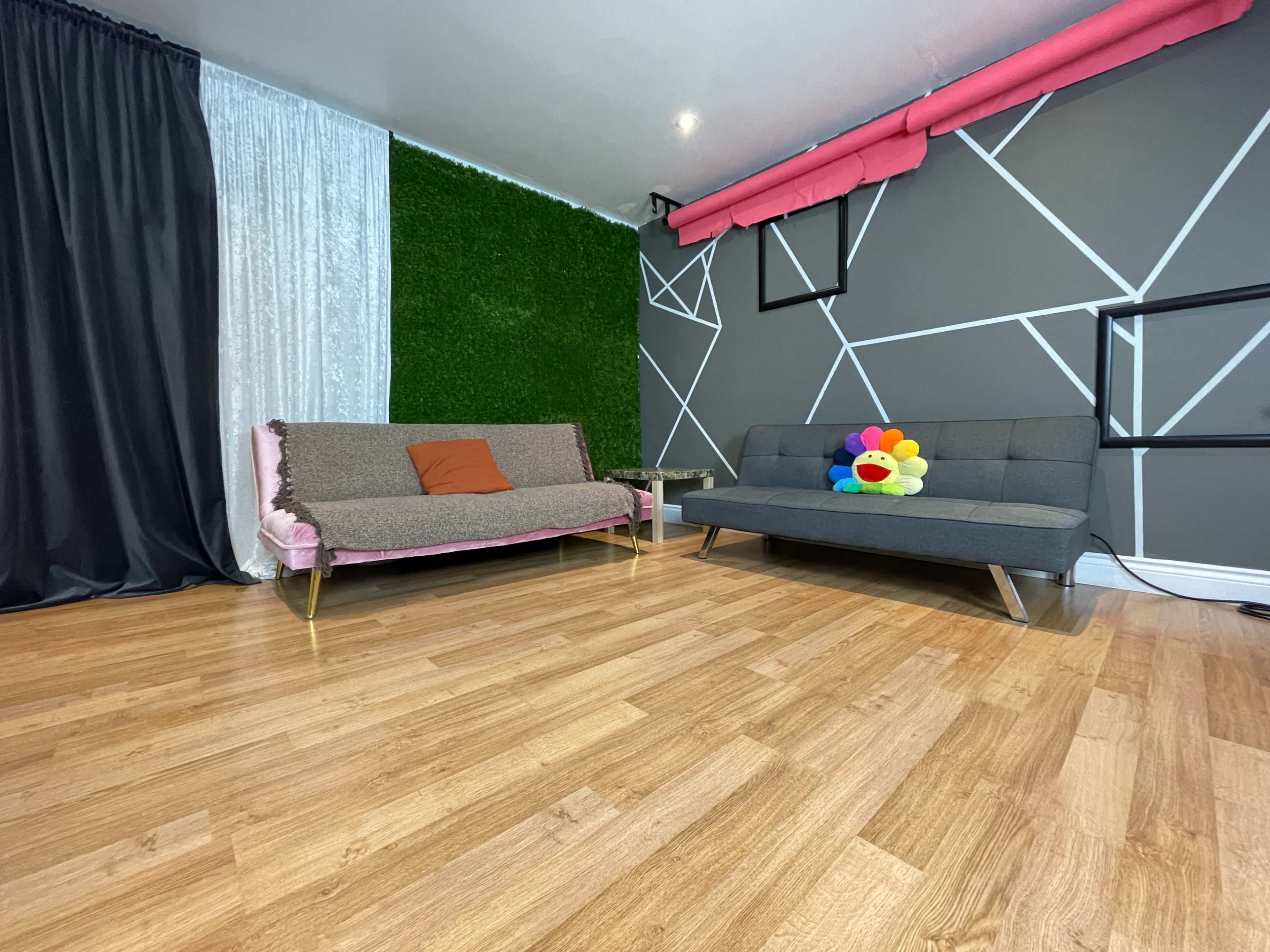 The scene features a modern living space with two sofas, one adorned with a colorful pillow, and a green accent wall, all set against a backdrop of geometric patterns.
