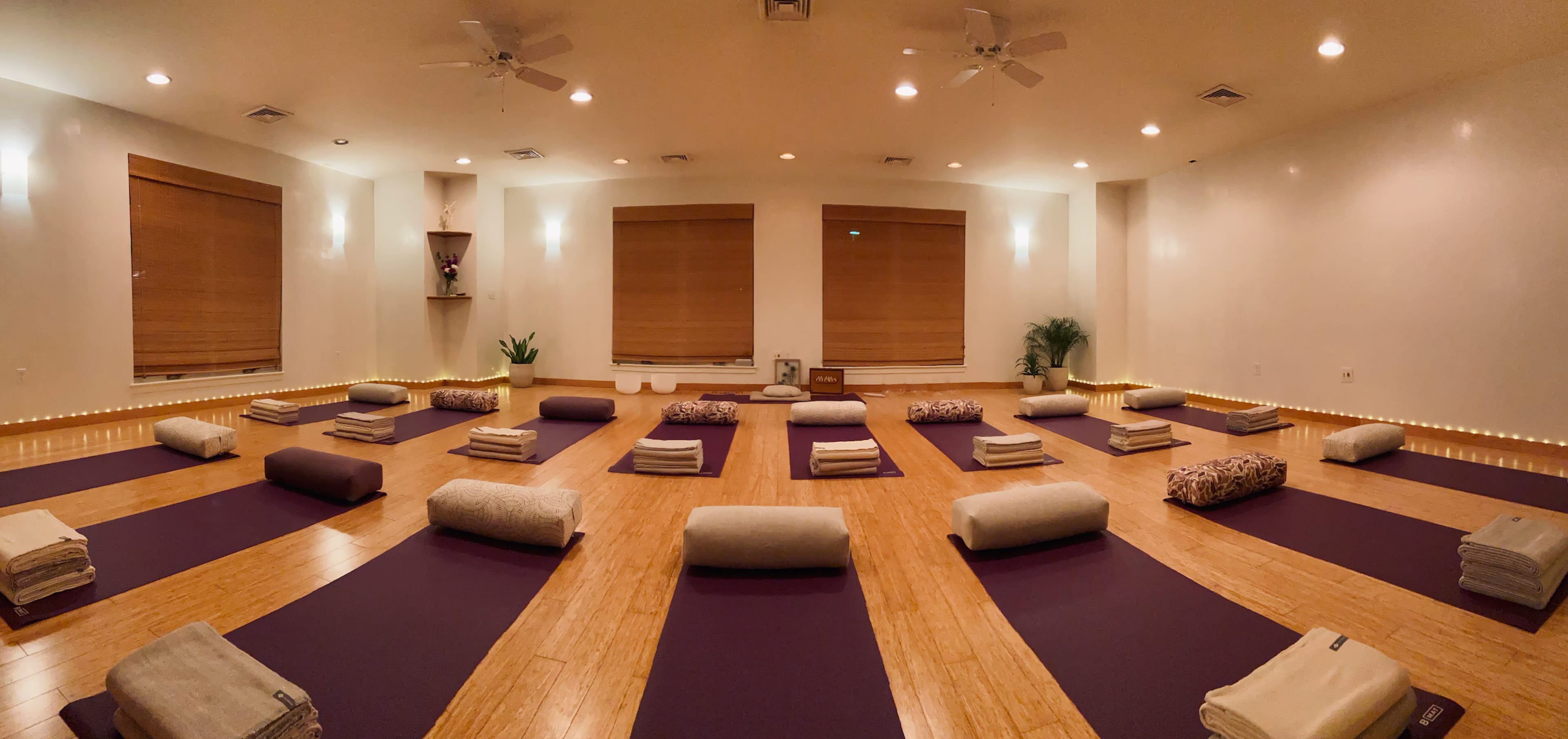 A spacious yoga studio arranged with mats and bolsters set up in a symmetrical pattern on a wooden floor.