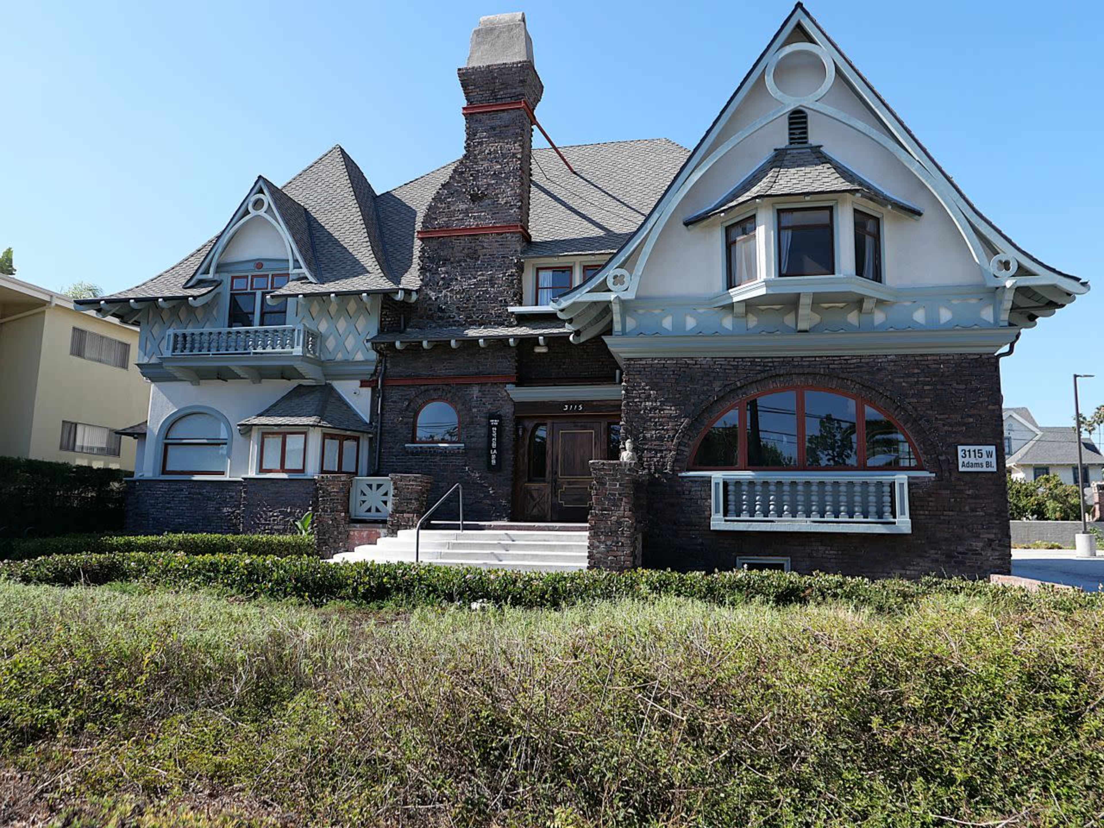 The image shows a large, Victorian-style house with a dark brick exterior, multiple gabled roofs, and decorative windows.