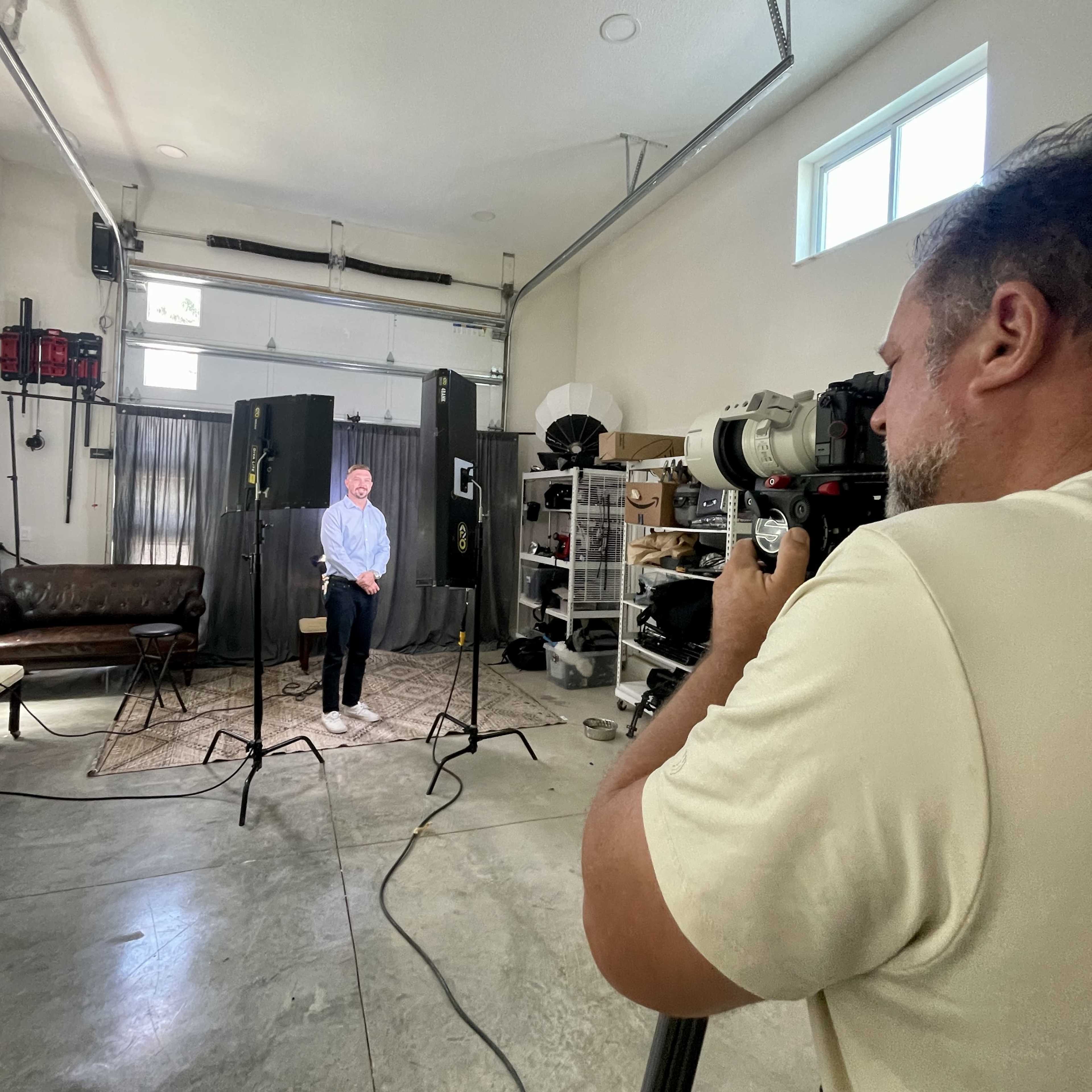 A photographer captures a portrait of a man sitting in a studio set up with lighting equipment.