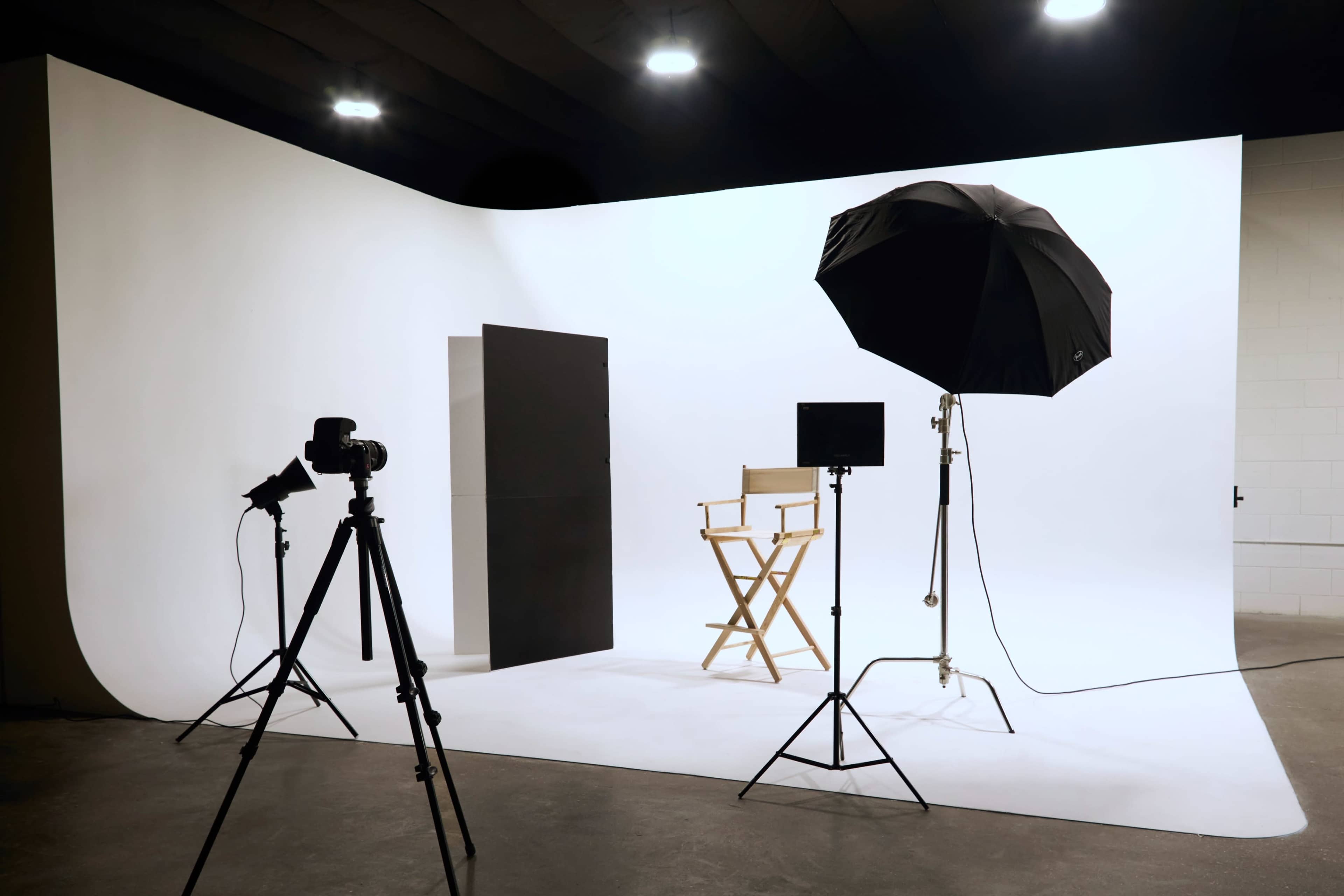 A photography studio is set up with a black backdrop, a director's chair, and lighting equipment.