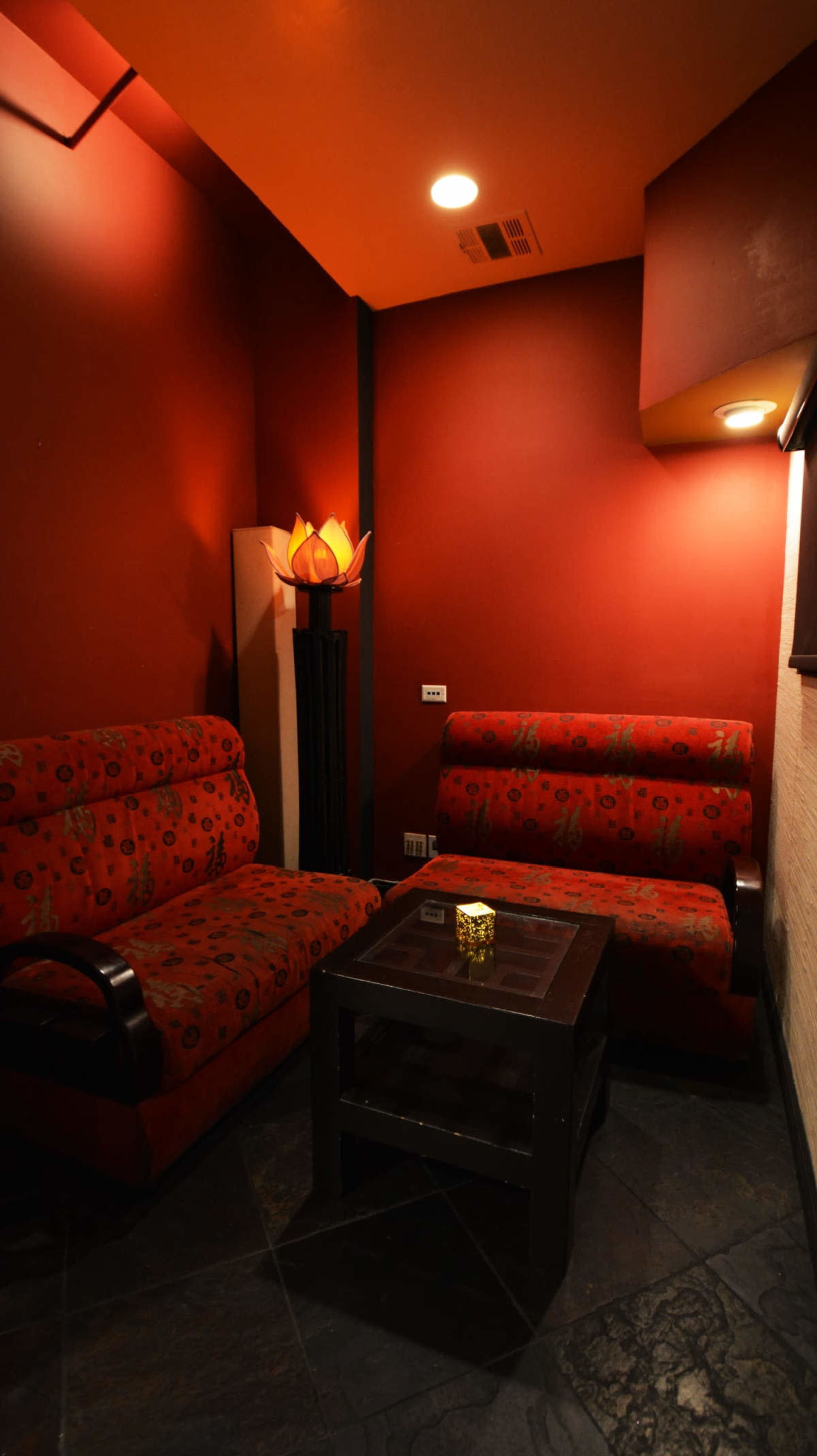 A small, cozy seating area with two patterned chairs, a dark table, and warm lighting against red walls.
