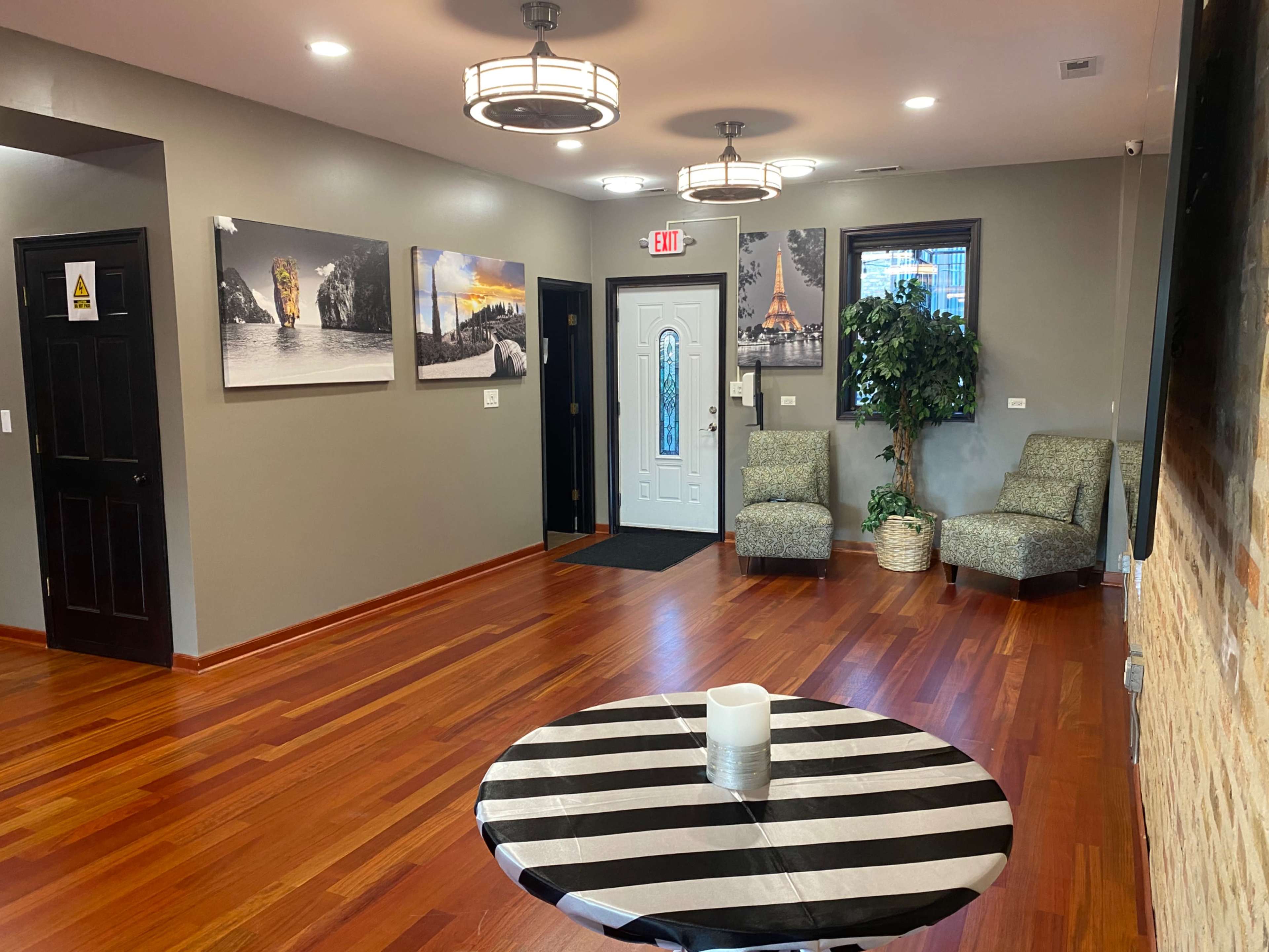 A welcoming interior space featuring hardwood floors, two upholstered chairs, a round table with black and white stripes, and several framed photographs on the walls.
