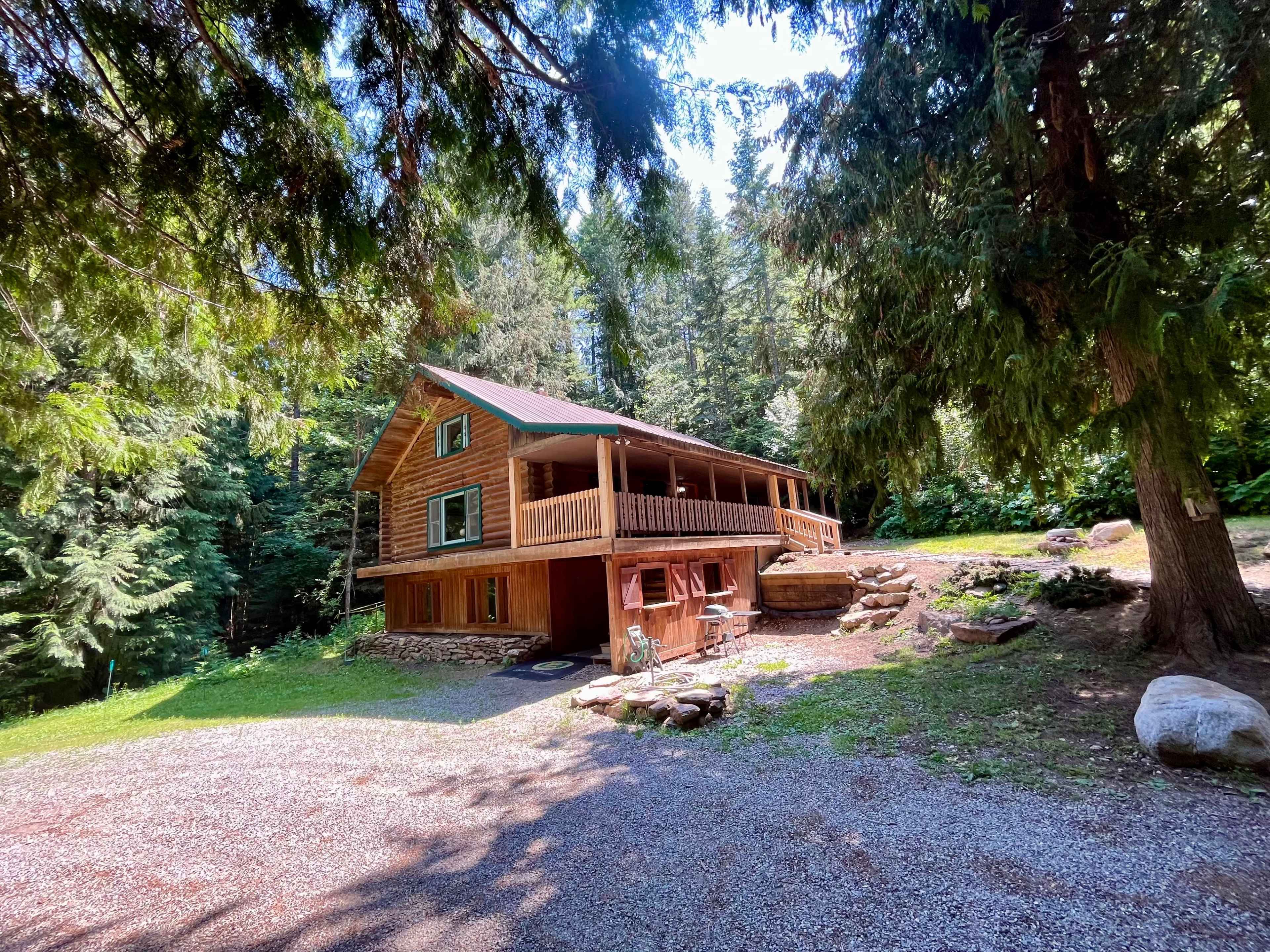 A wooden cabin with a porch is situated among tall trees in a forested area.