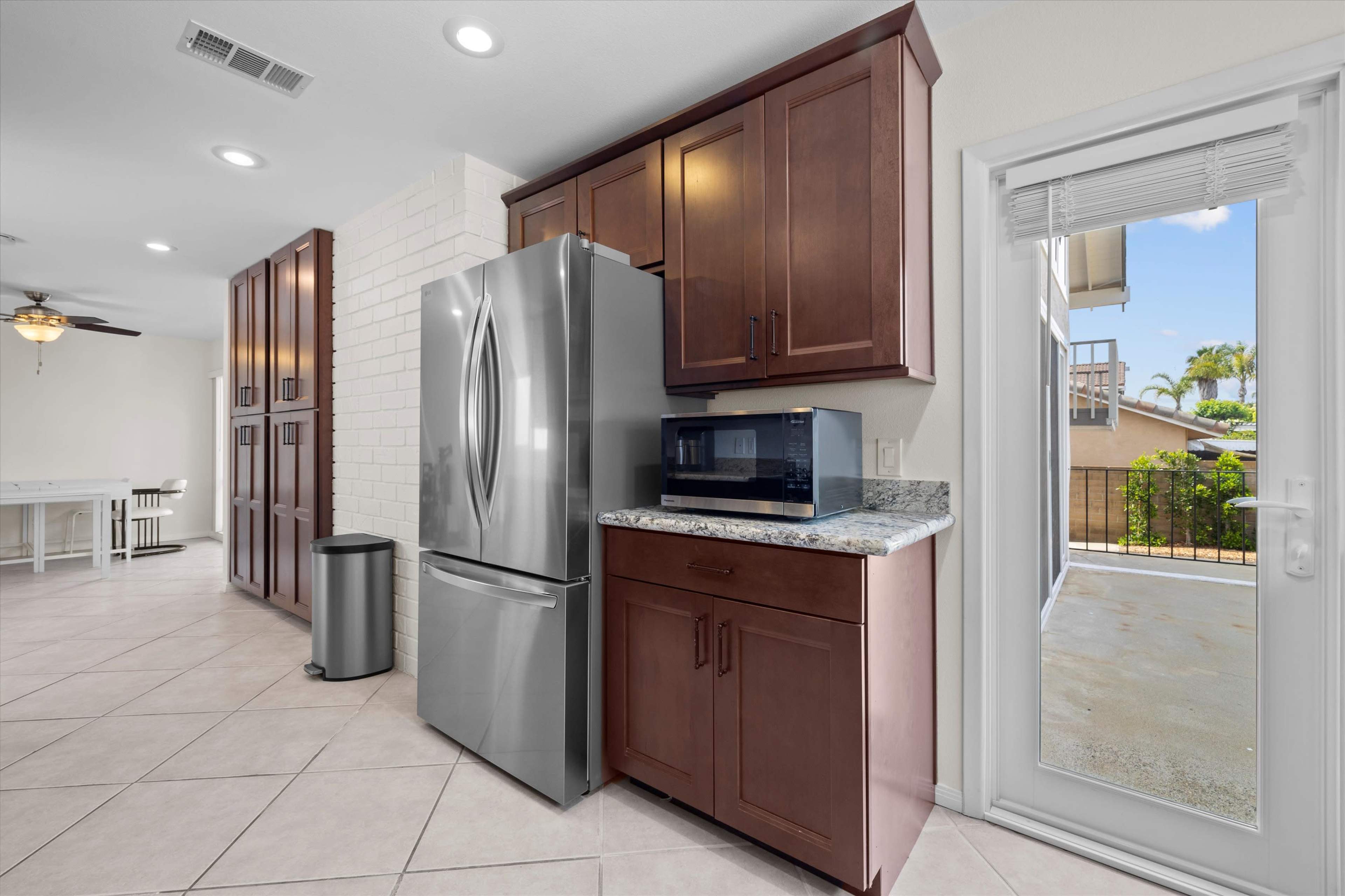 A kitchen area features a stainless steel refrigerator and microwave against dark wood cabinetry, with a door leading to an outdoor space.
