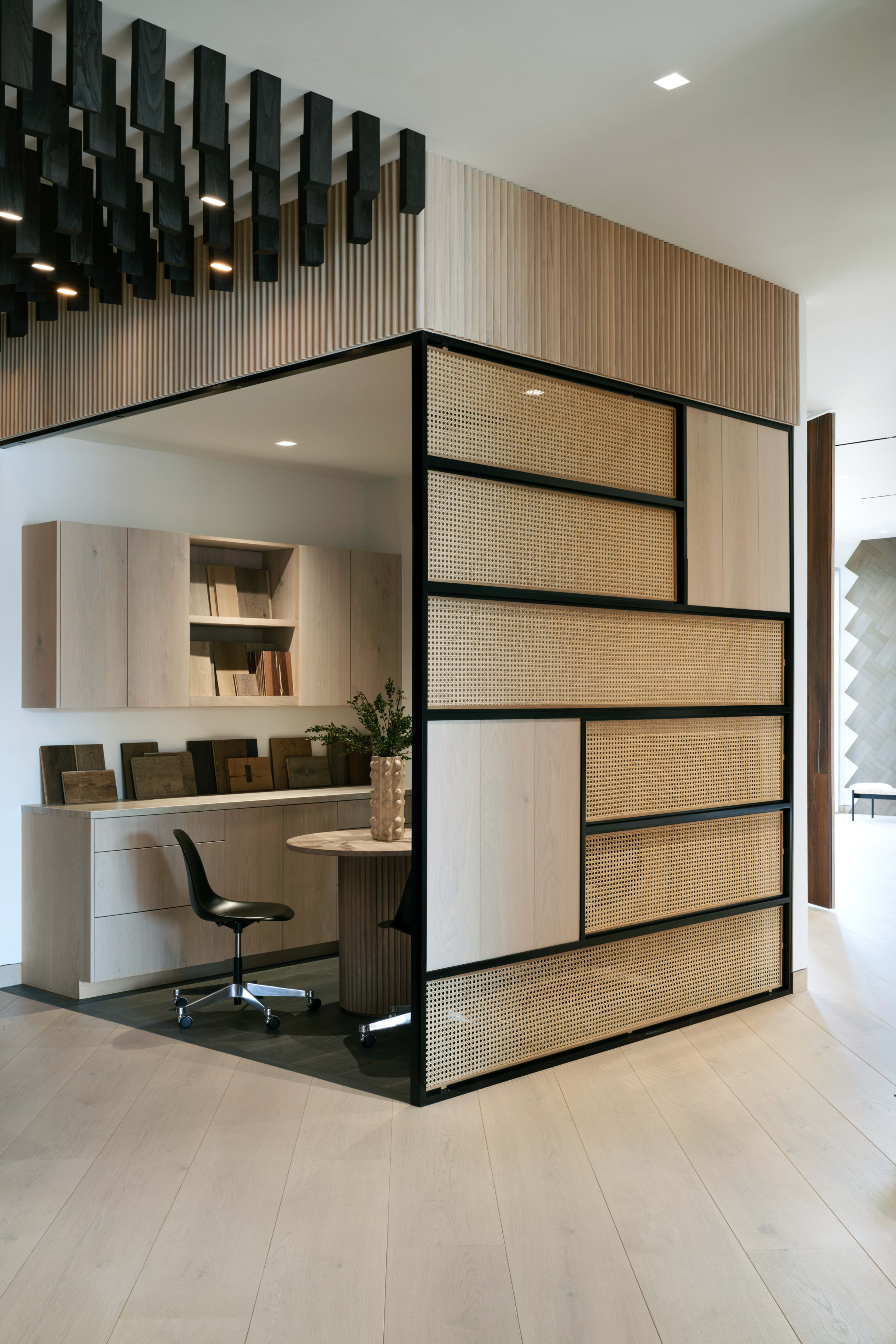 A modern office space features a combination of wood paneling and a patterned divider, with a desk, chair, and shelves in an organized layout.