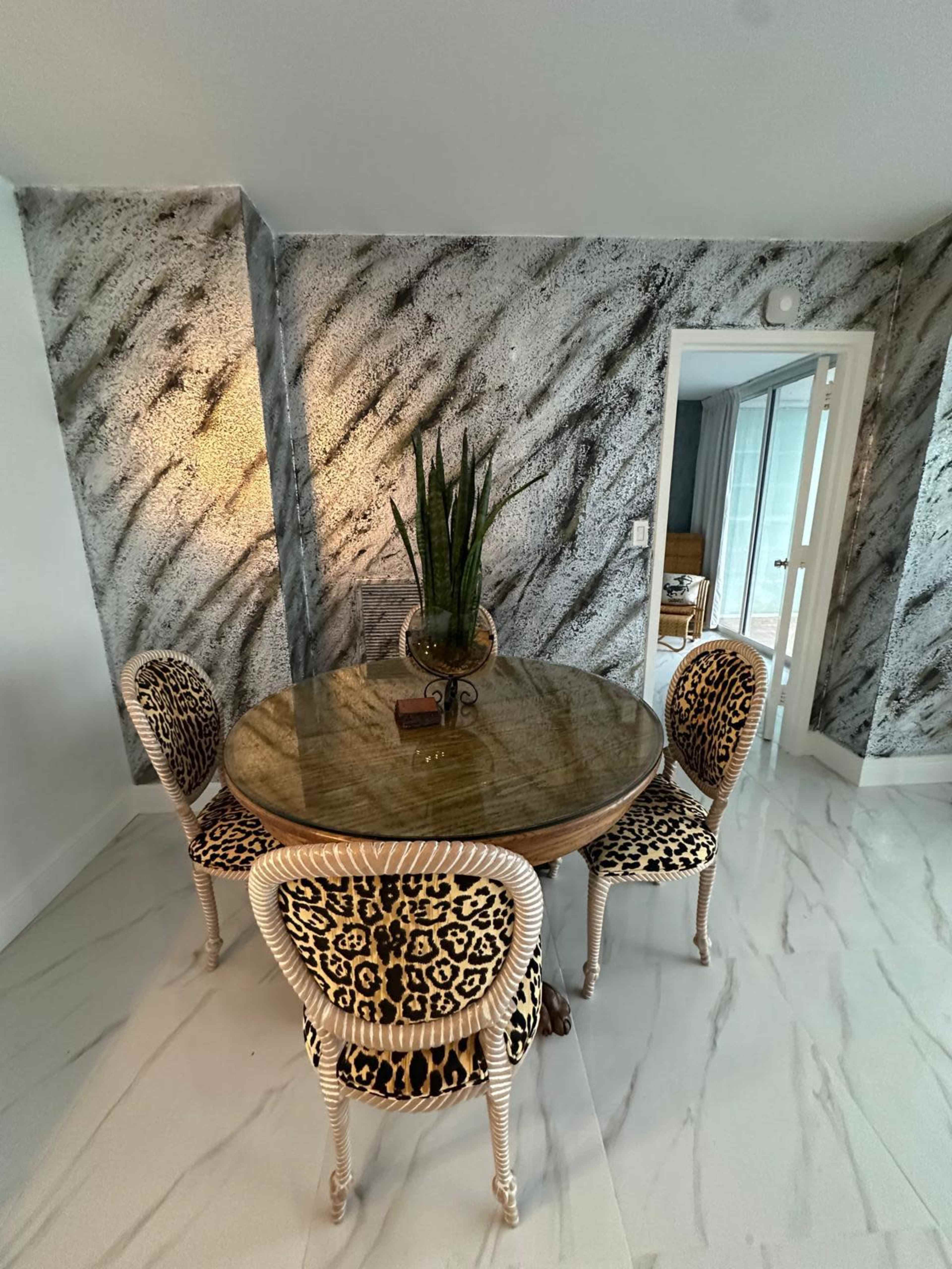 A round table surrounded by four leopard-print chairs is set against a textured, patterned wall in a well-lit dining area.