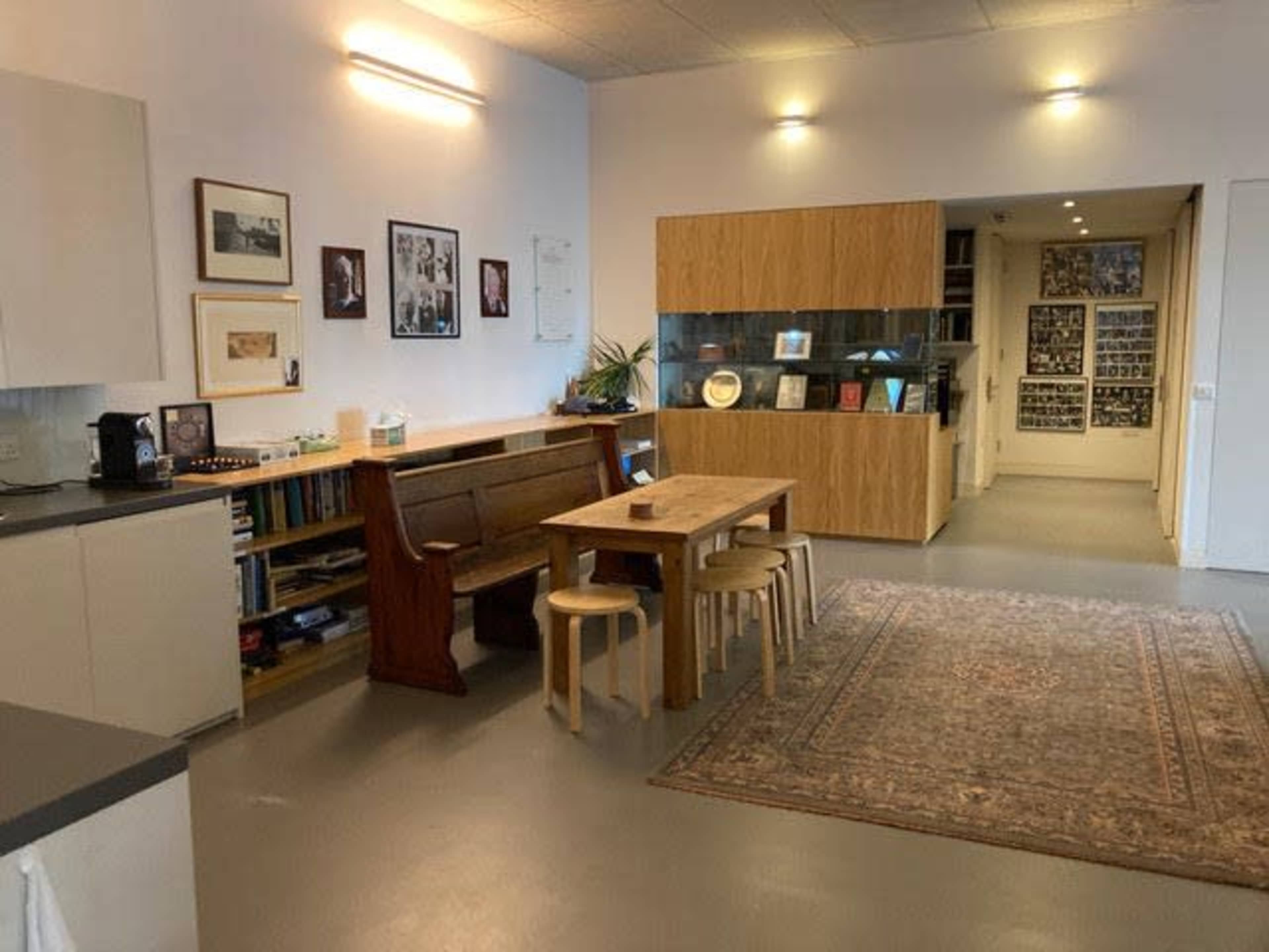 A spacious interior with a wooden dining table surrounded by stools, a modern cabinetry unit, and framed photographs on the walls.